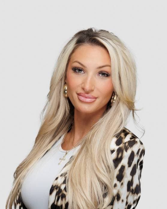 Blonde woman in a leopard-print jacket and white top, posing against a light gray background.