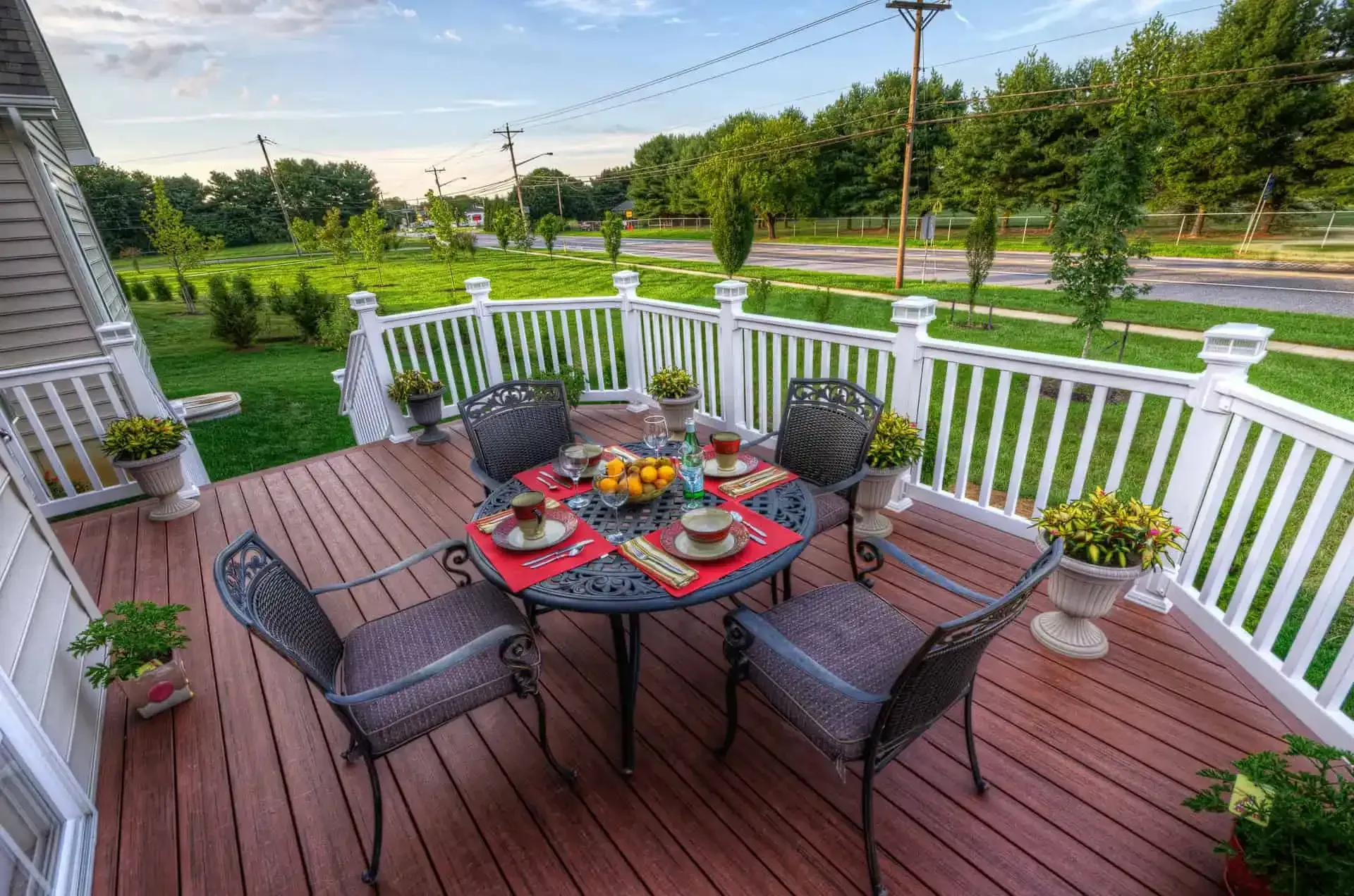 Patio deck with a dining table set for breakfast, surrounded by white railing and overlooking a green lawn