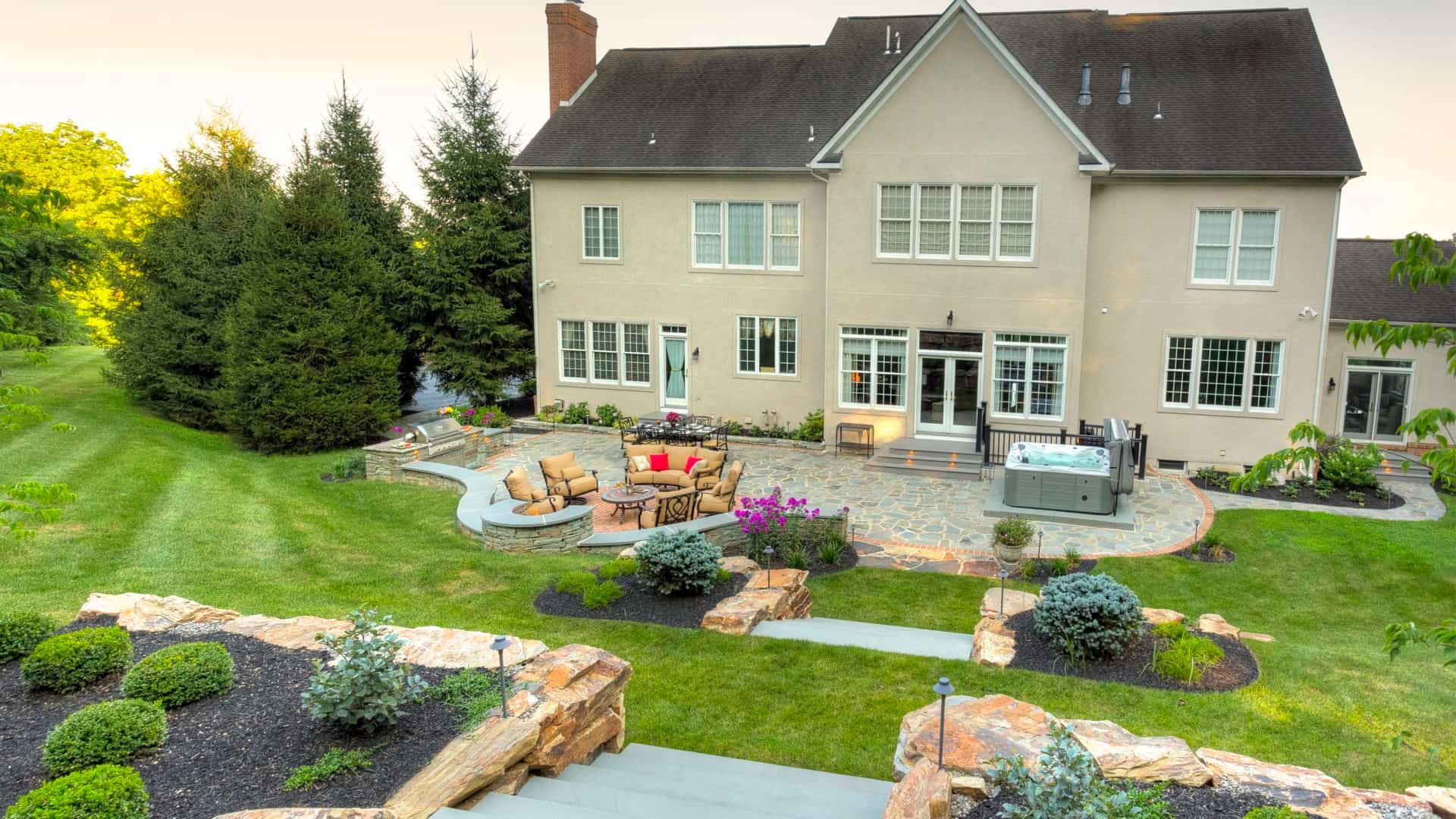 Backyard patio with lawn, flower beds, stone path, and a two-story beige house