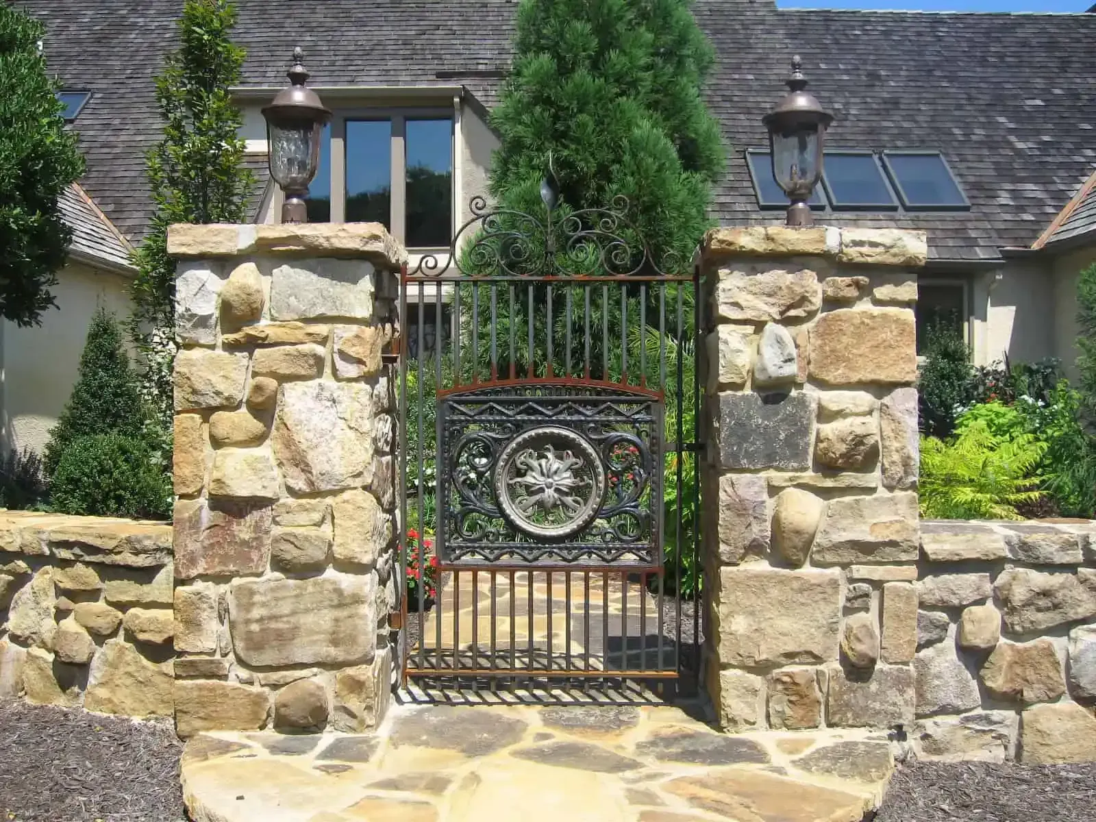 Stone gate with wrought-iron door and circular emblem in front of a house with ivy-covered walls