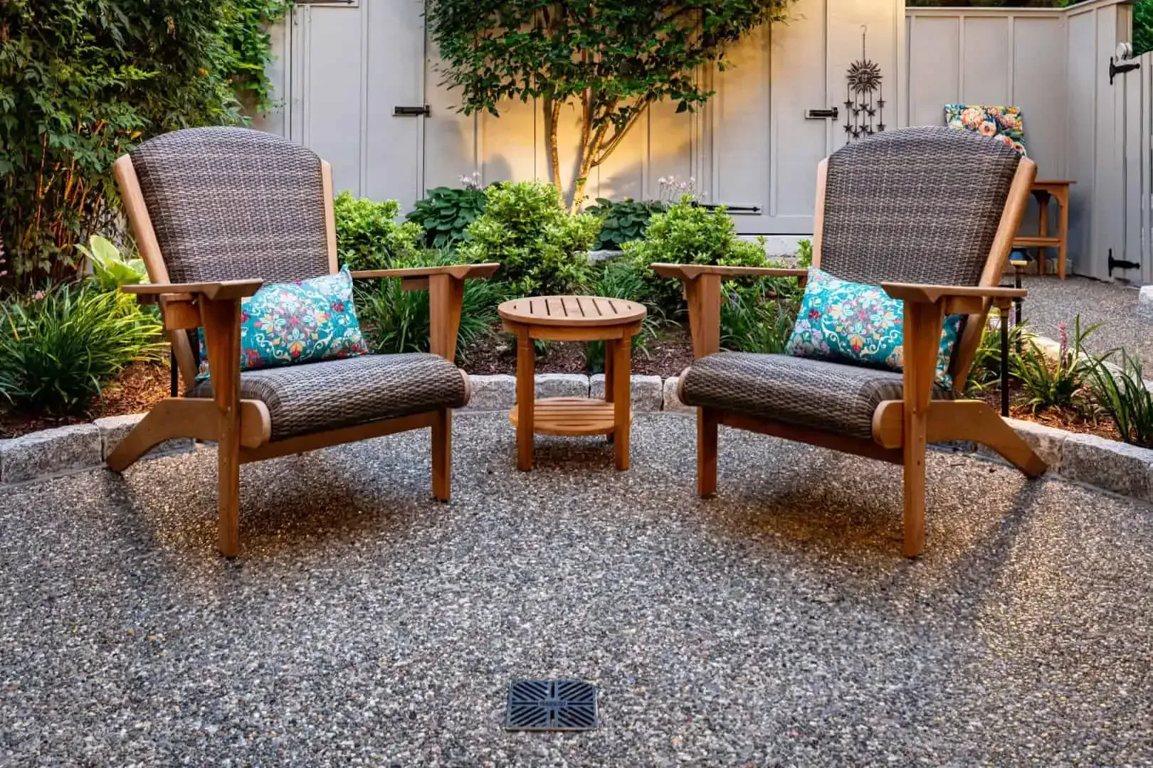 Two wicker chairs with colorful pillows and a small table in a sunny garden patio