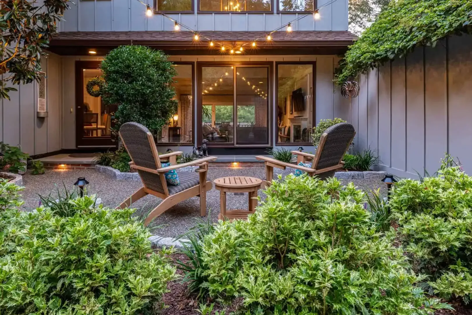 Cozy backyard patio with wicker chairs, fire pit, and lush greenery outside a modern home
