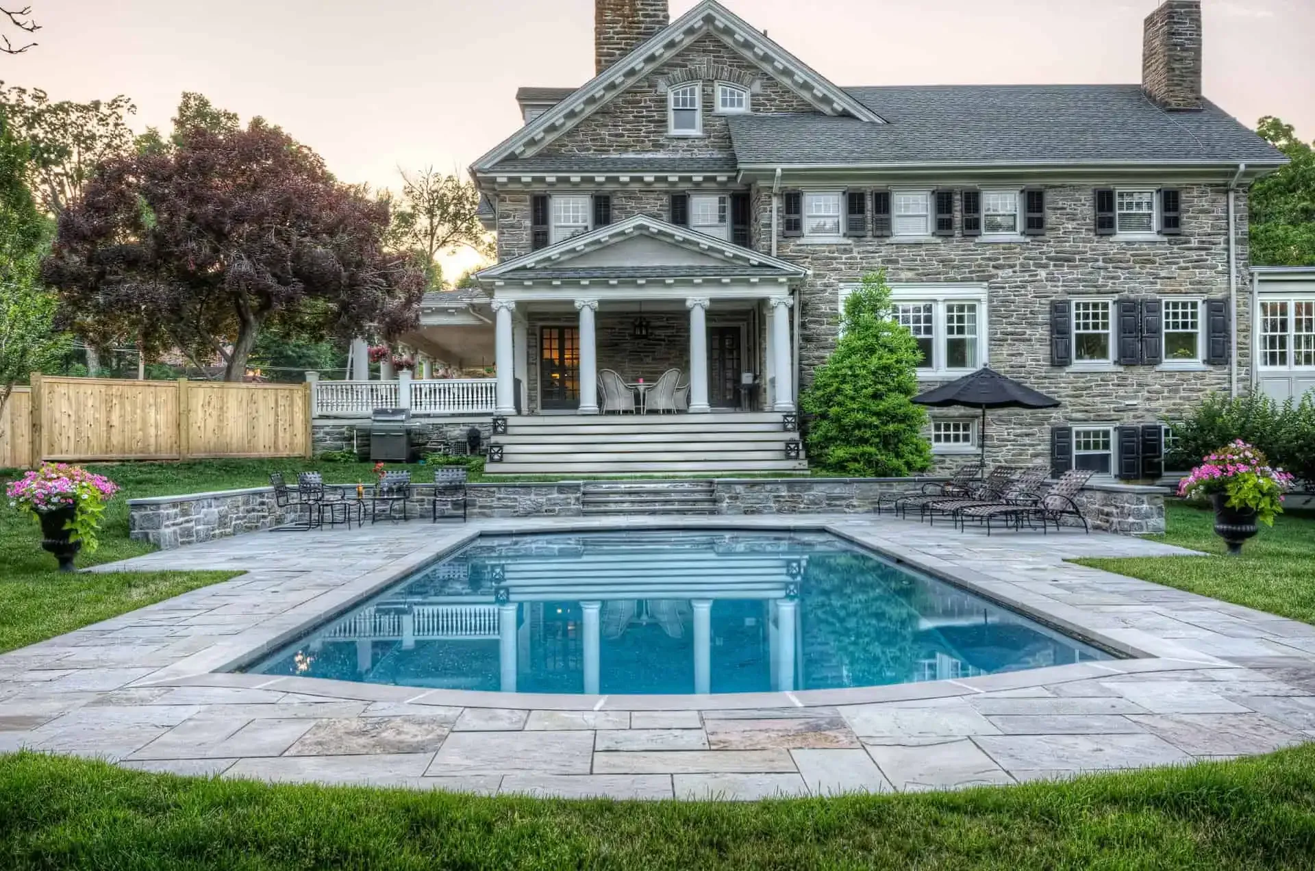 Stone house with a covered porch and a backyard swimming pool at dusk