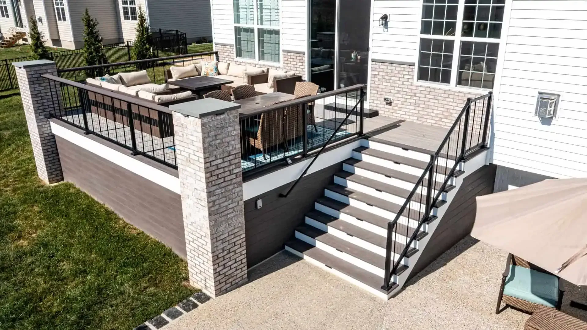 Elevated backyard deck with patio furniture, black railings, and stairs leading to a brick house