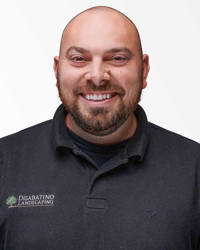 Smiling bald man with a beard in a dark gray polo shirt against a white background