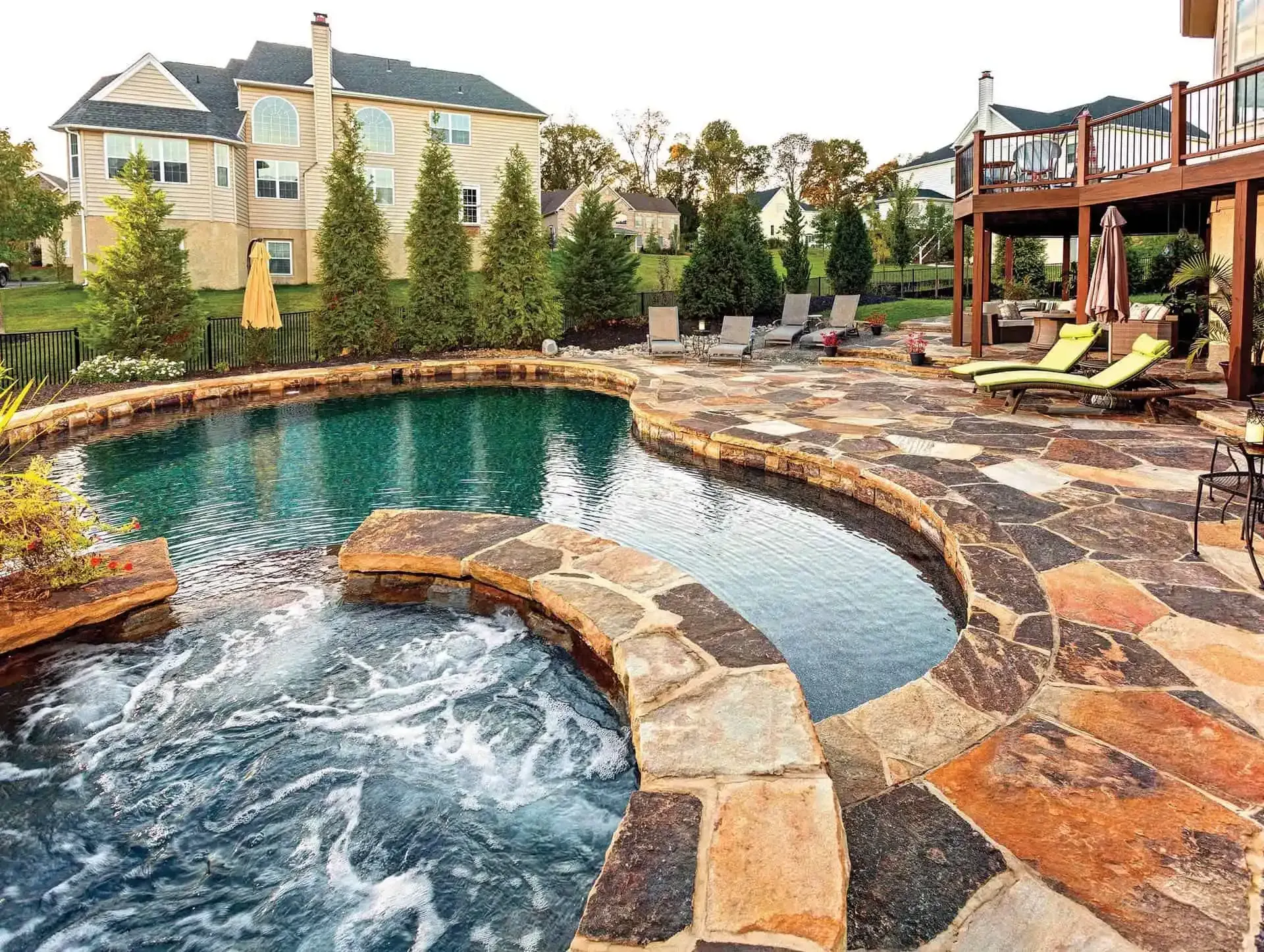 Backyard pool with hot tub, stone deck, lounge chairs, and apartment buildings in the background