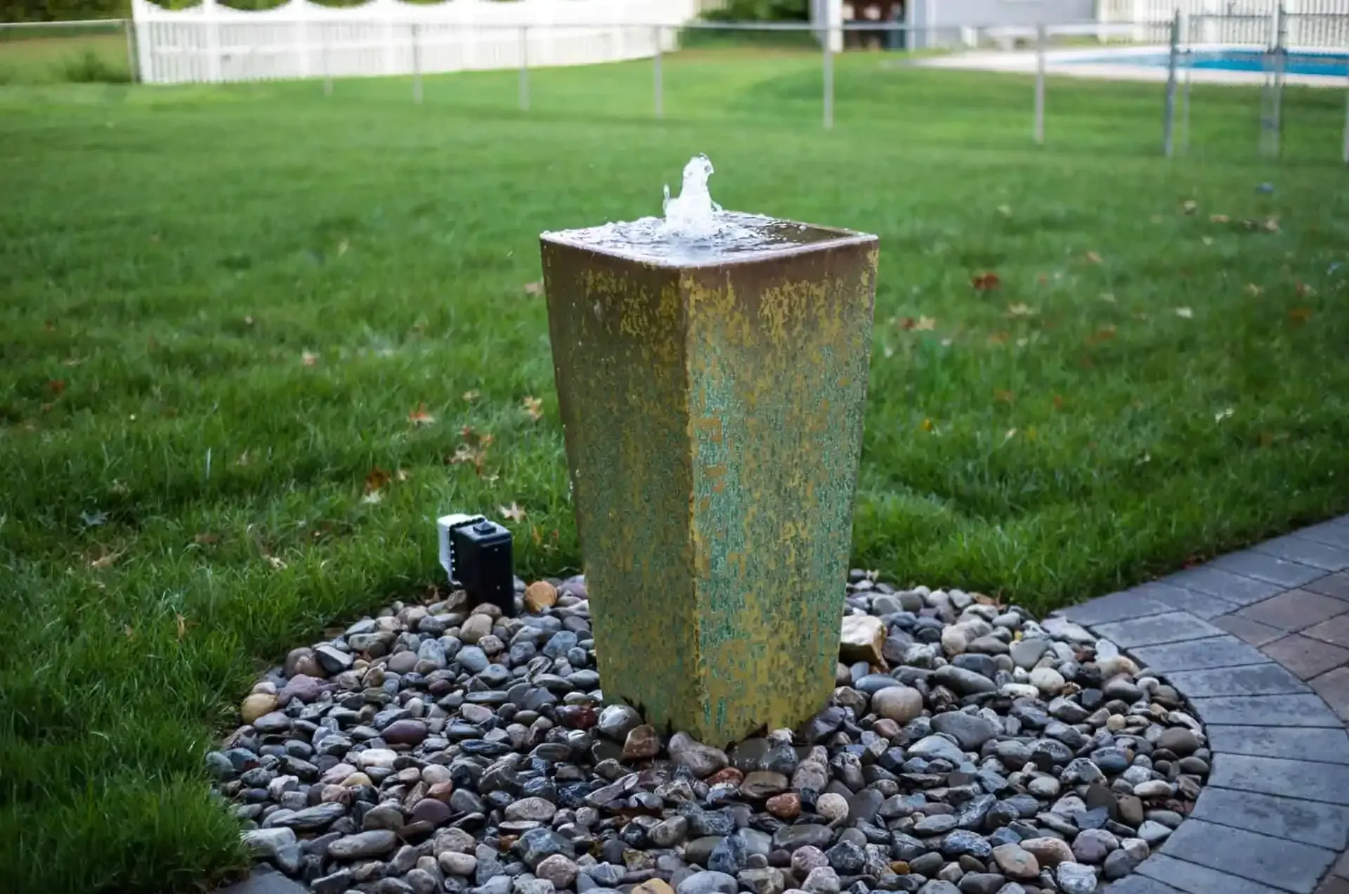Small outdoor fountain on a stone bed in a grassy yard, water bubbling from the top.