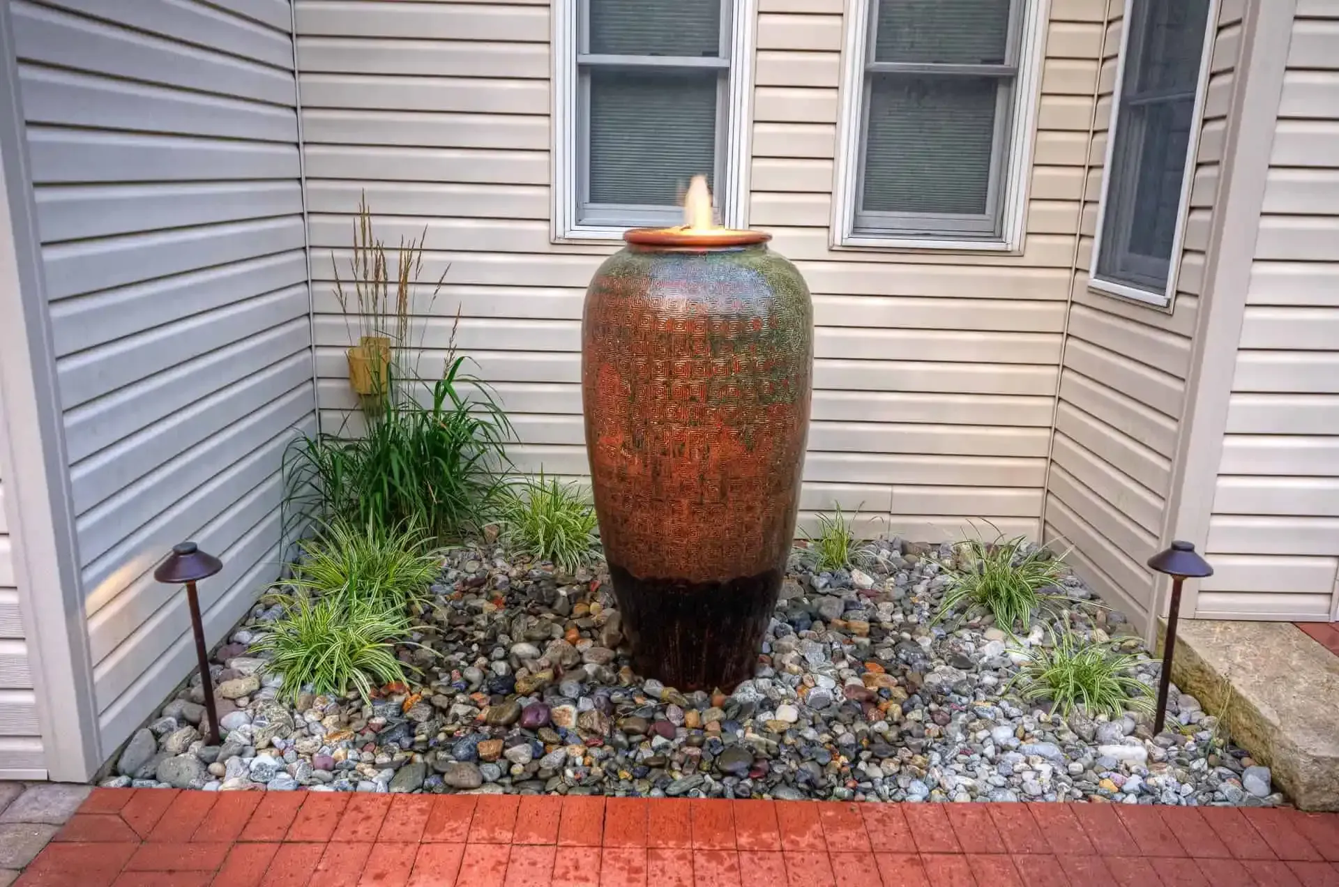 Decorative ceramic water fountain in a gravel courtyard between beige siding walls