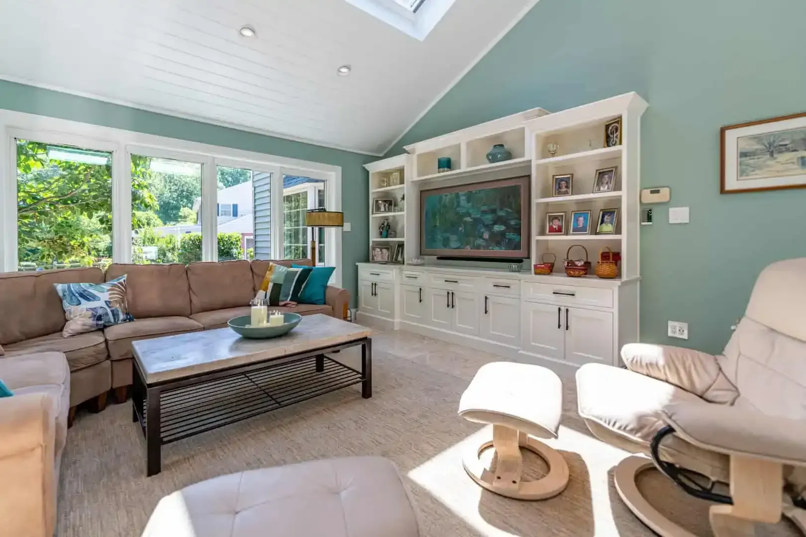 Bright living room with sectional sofa, white built-in TV cabinet, and large windows on a vaulted ceiling
