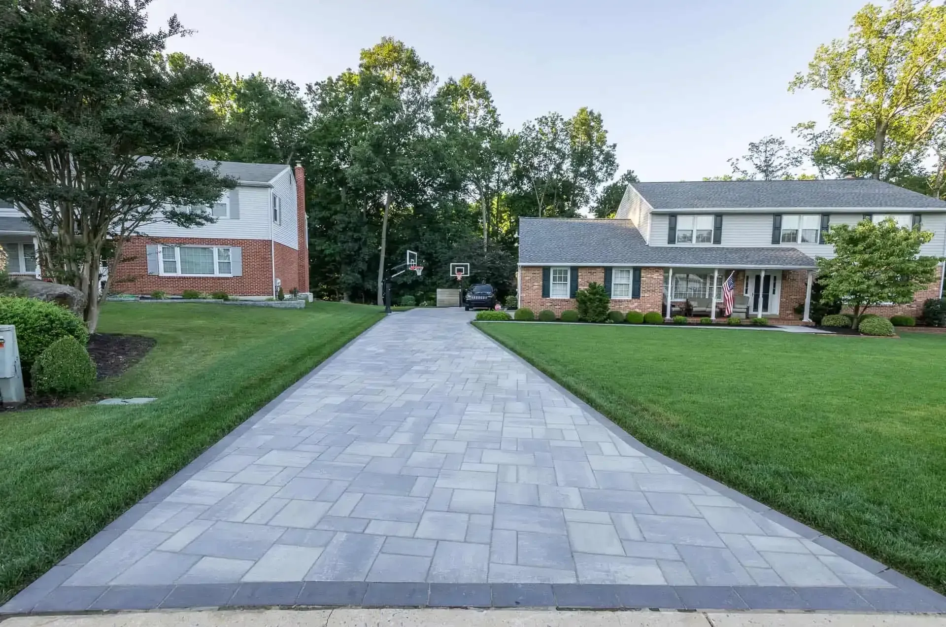 Long paved driveway between two suburban houses with green lawns and trees