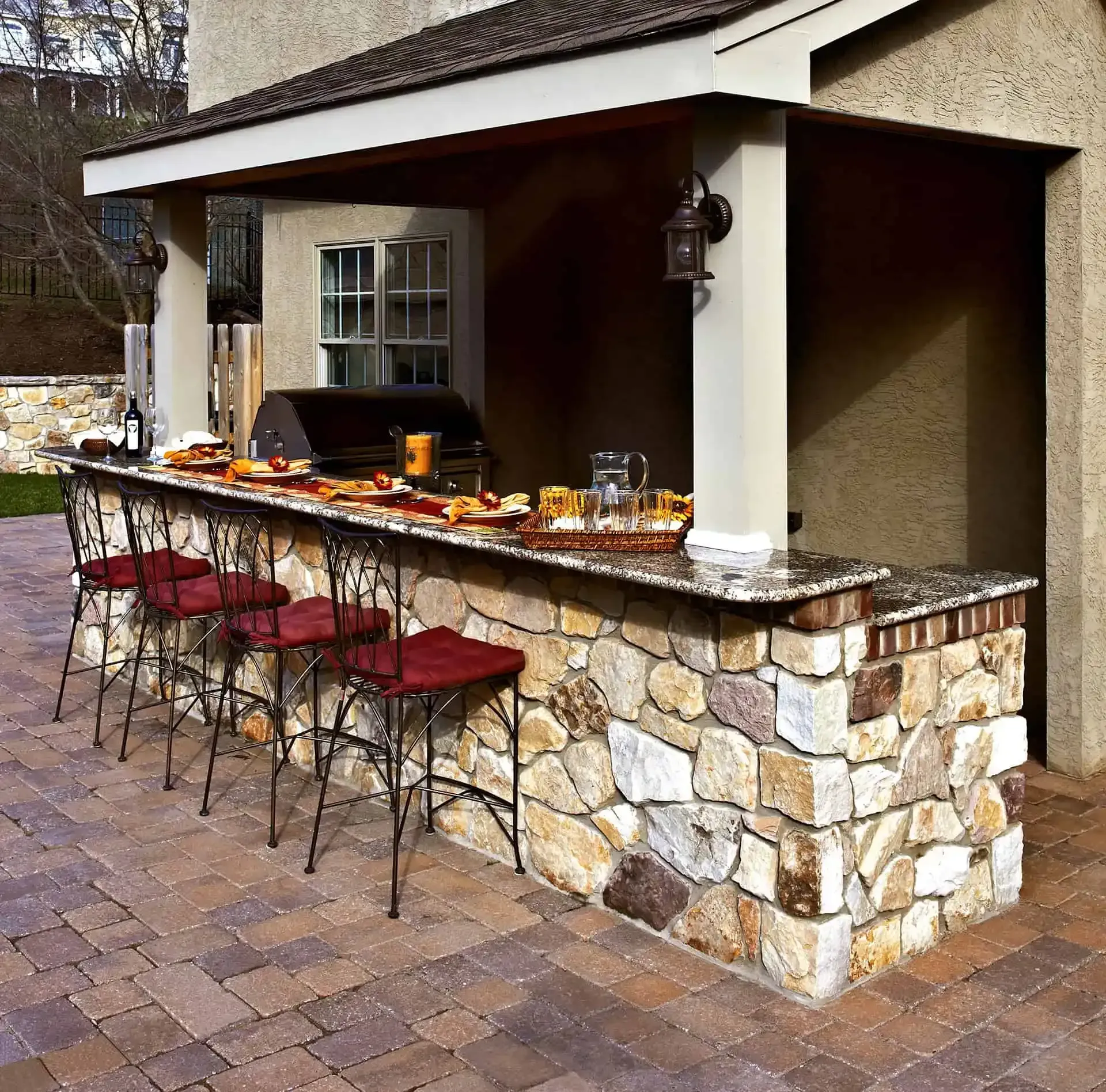 Stone outdoor bar with red stools, a dark countertop, and a covered serving area.