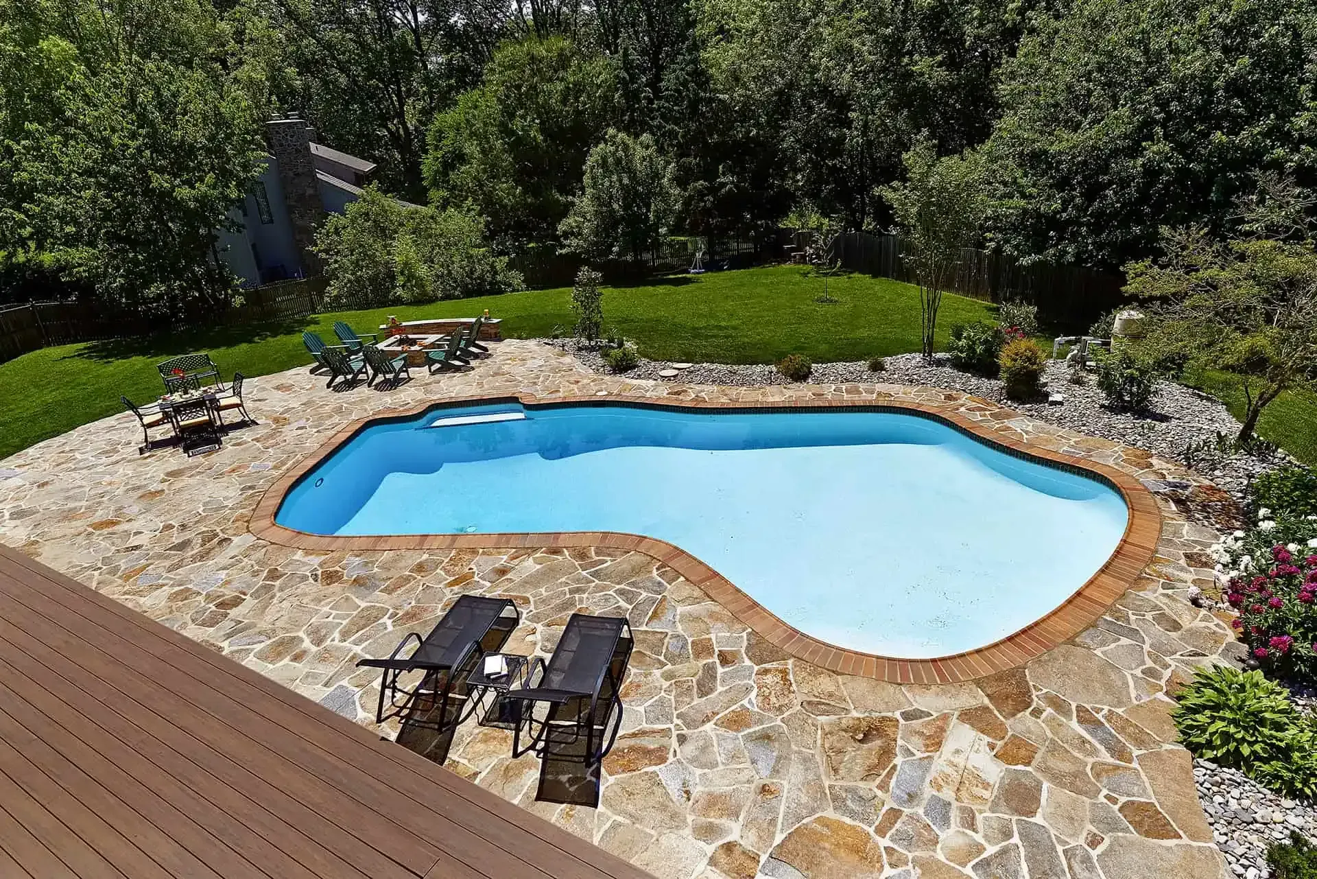 Backyard swimming pool with stone patio, lounge chairs, and lush green trees