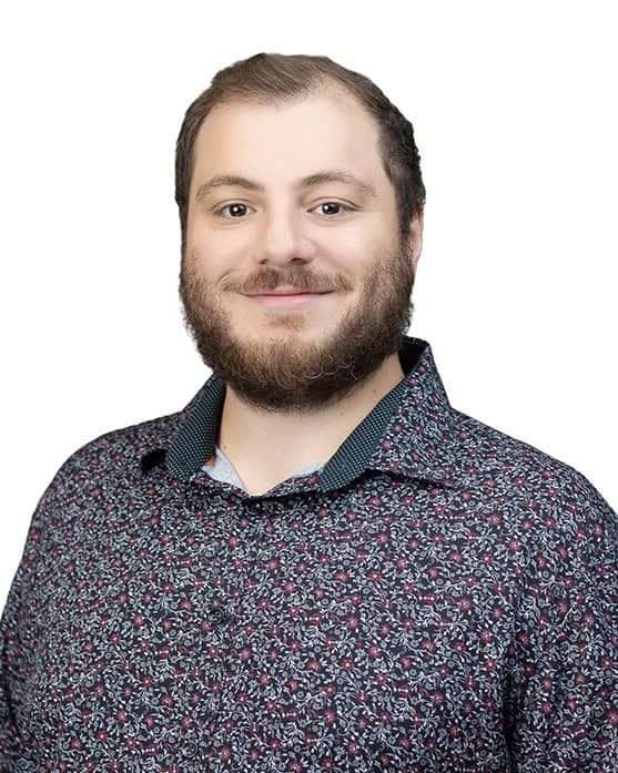 Smiling bearded man in a patterned dark shirt against a white background