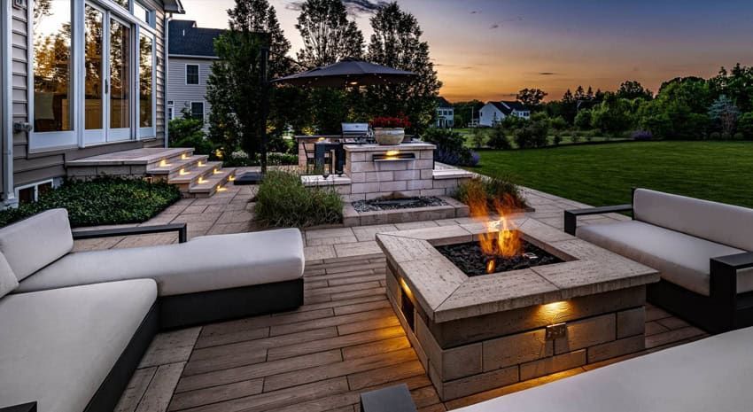 Modern backyard patio at dusk with fire pit, seating, and landscaped garden near a house