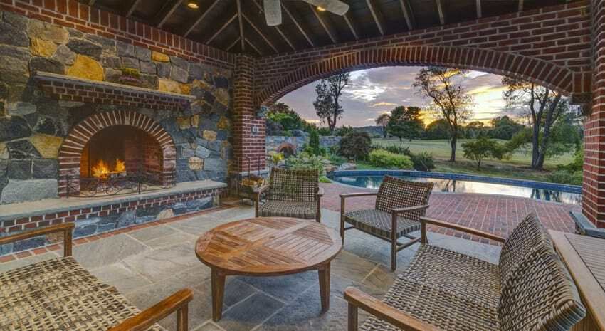 Covered patio with wicker chairs and round table overlooking a pool and sunset view.