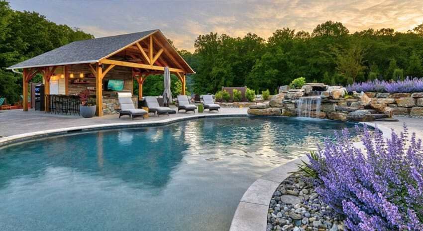 Luxury resort pool with a stone edge, cabana, loungers, and purple flowers at sunset.