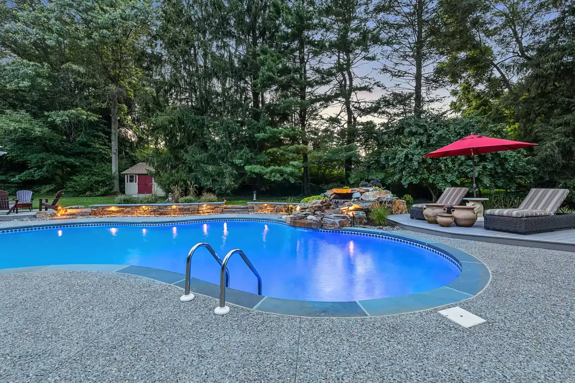 Outdoor pool with blue water, lounge chairs, and a red umbrella surrounded by trees