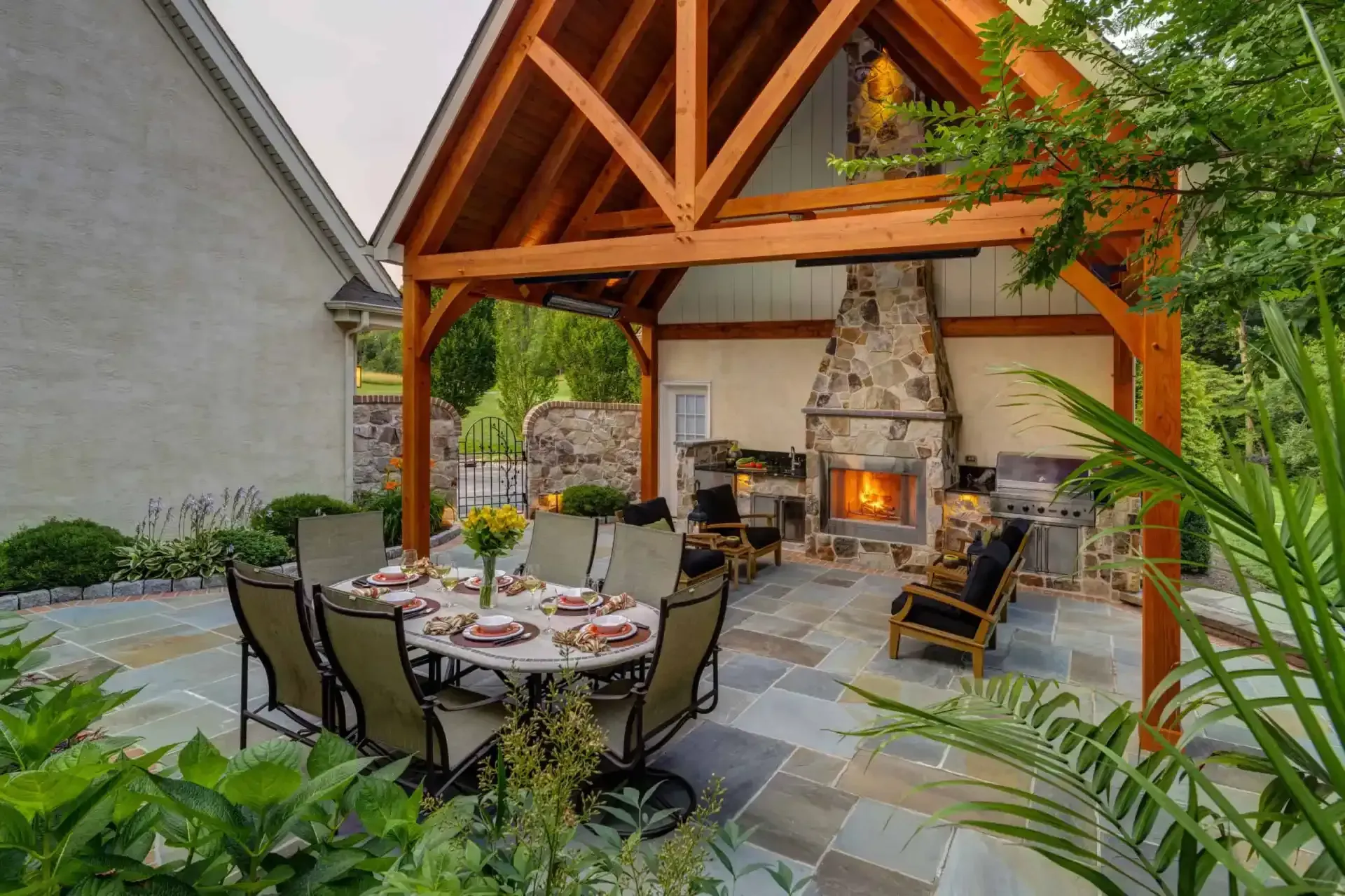Outdoor patio dining area with stone fireplace, wooden beams, and a round table set for guests