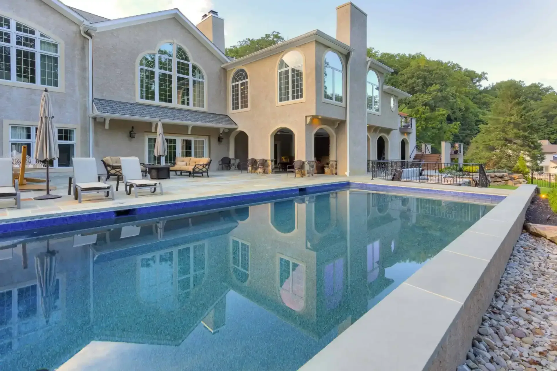 Modern house with a rectangular backyard pool and patio seating, reflecting the home at dusk