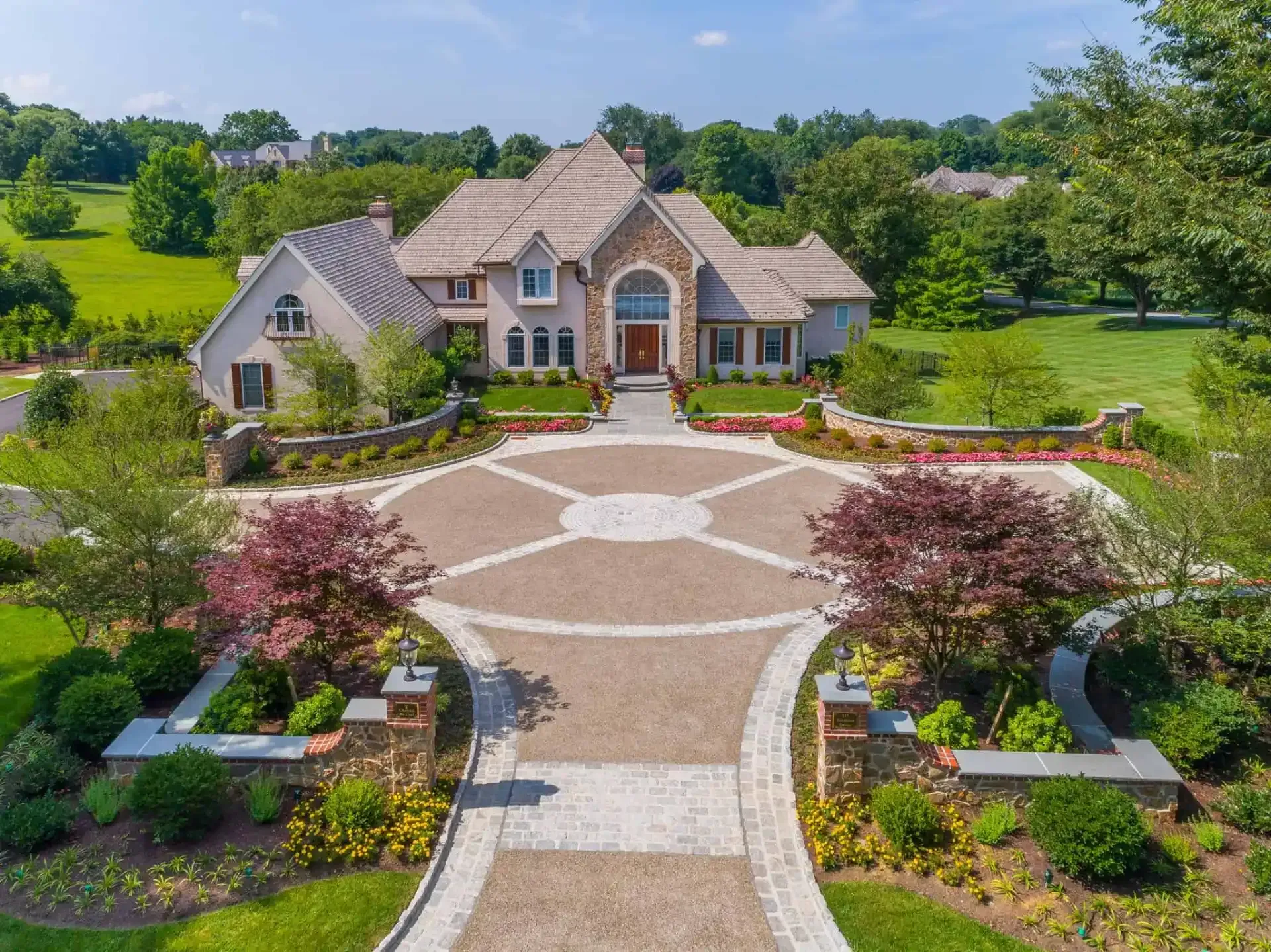 Large brick mansion with a circular driveway, landscaped gardens, and a broad stone walkway