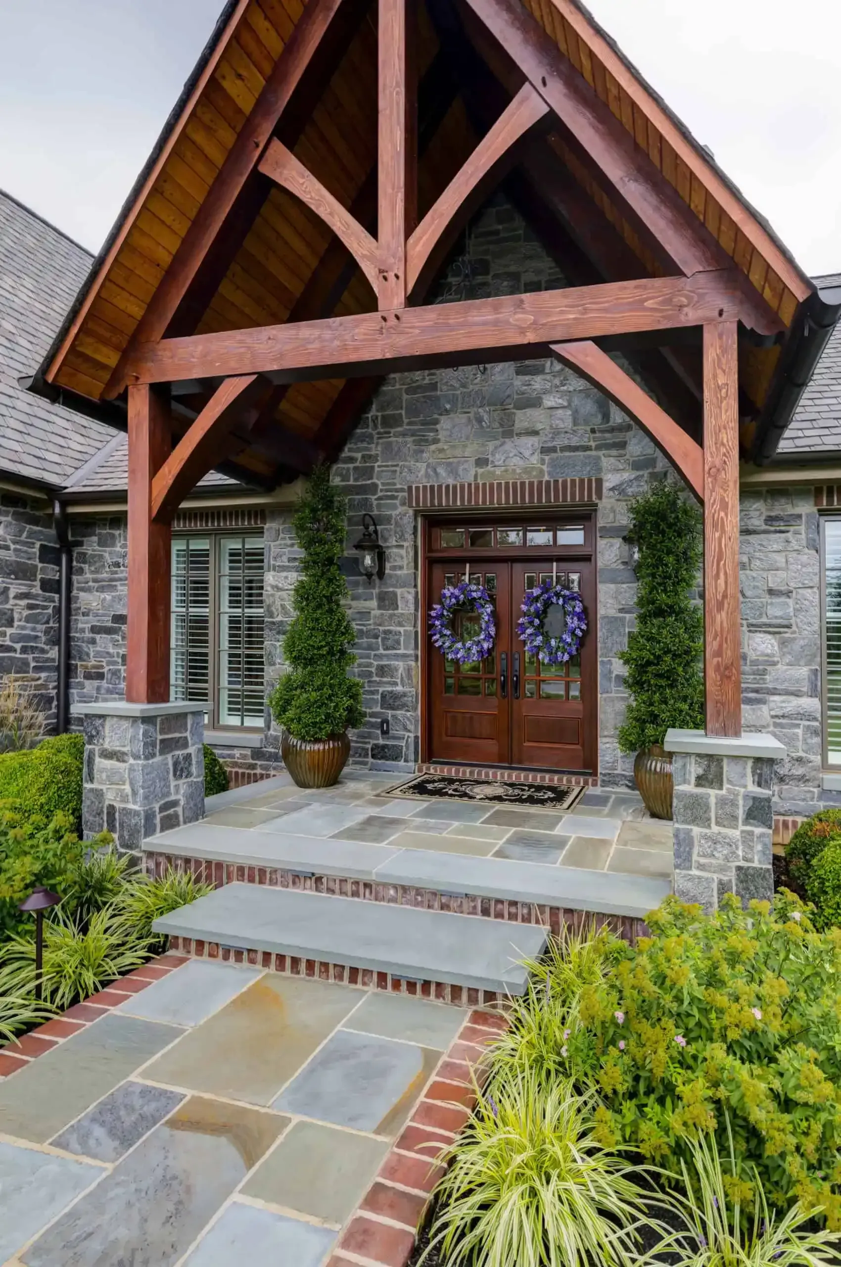 Stone house entrance with wooden gabled porch, double front doors, and slate walkway steps