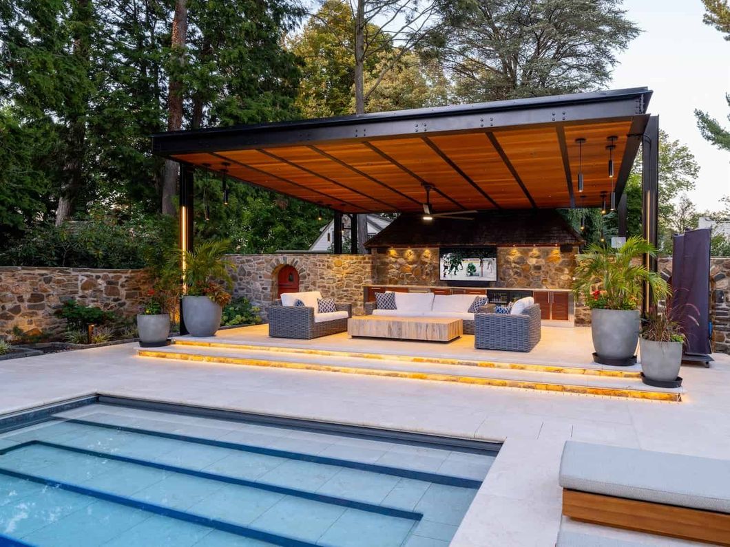 Modern backyard pool with covered outdoor lounge and fire pit at dusk