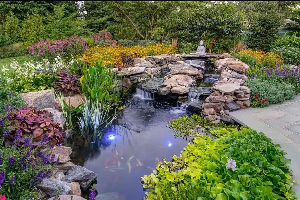 Garden pond with rock waterfall, colorful flowers, and lush greenery surrounding the water