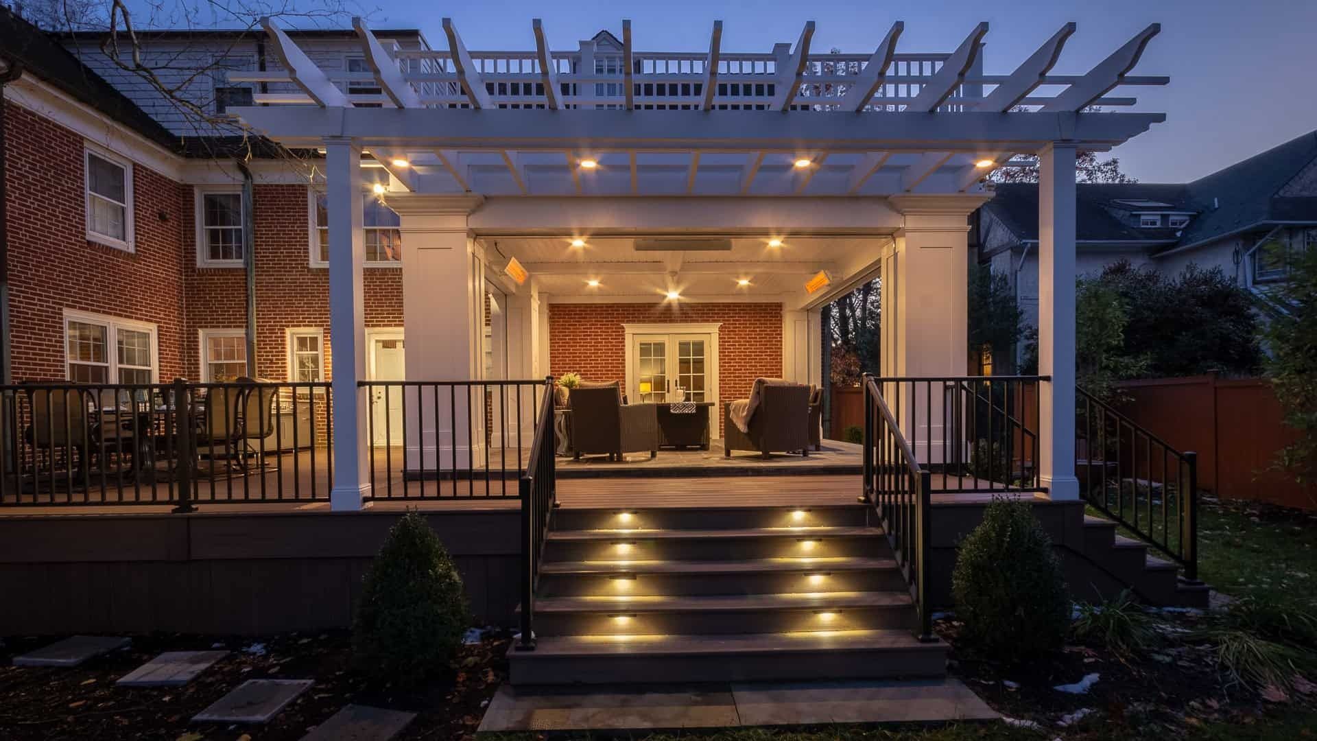 Covered backyard patio with lit steps, pergola, brick walls, and outdoor seating at dusk