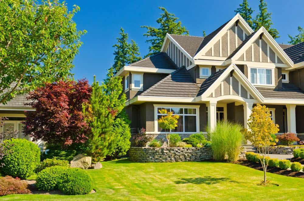 Suburban house with a manicured green lawn, trees, and bright blue sky