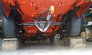 The rear end of an orange car is sitting on blocks in a garage.