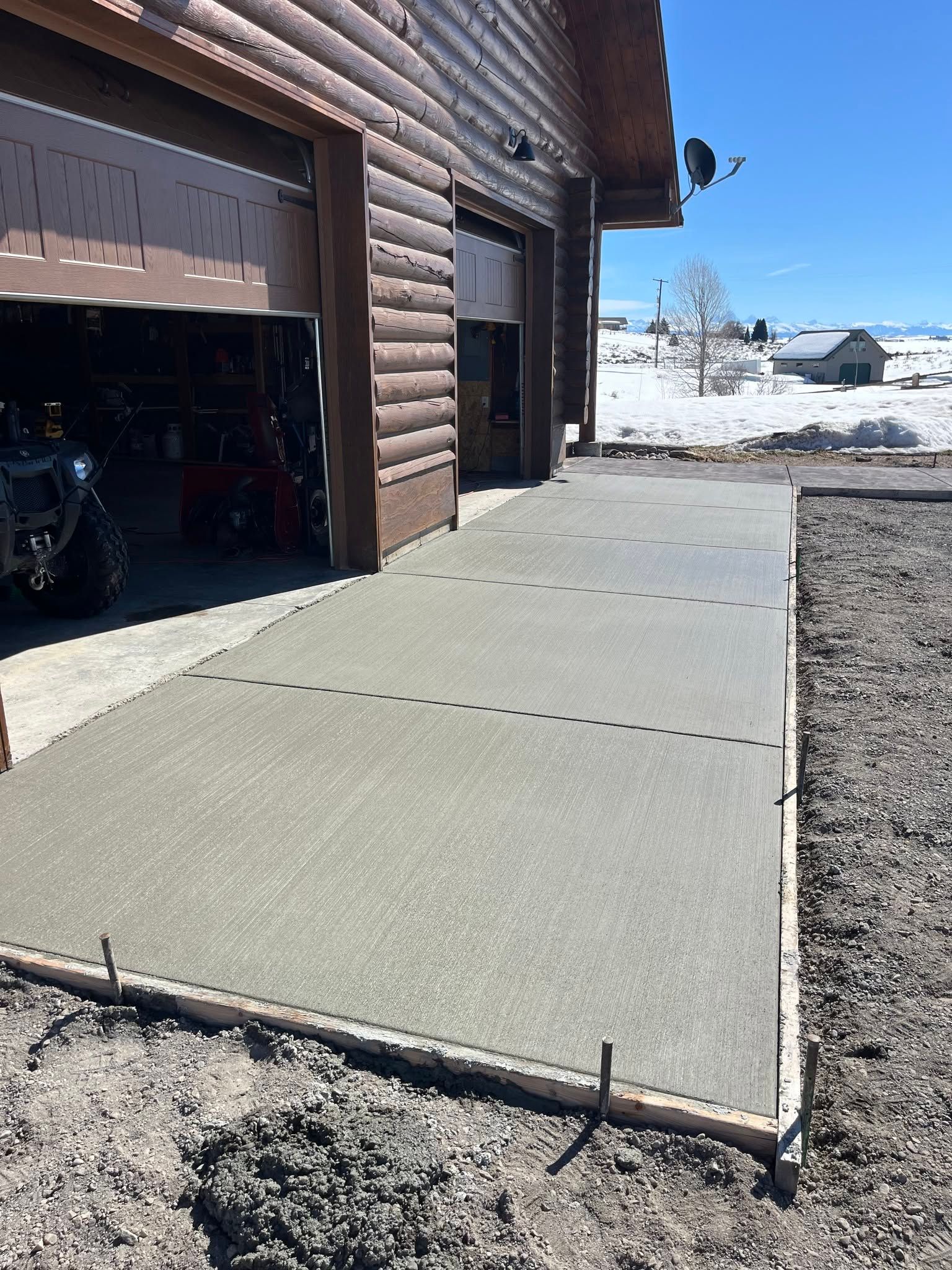 Concrete garage ramp beside brown house in snowy yard under a clear blue sky