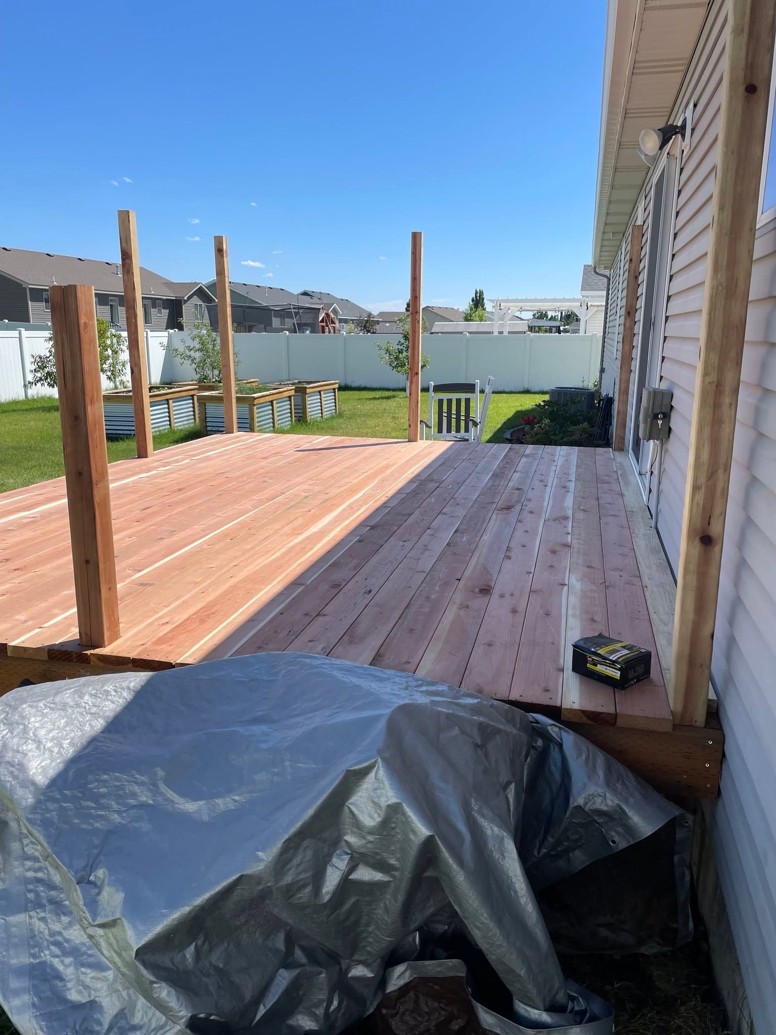 Wooden deck under construction beside a house, with railing posts and a tarp in the foreground.