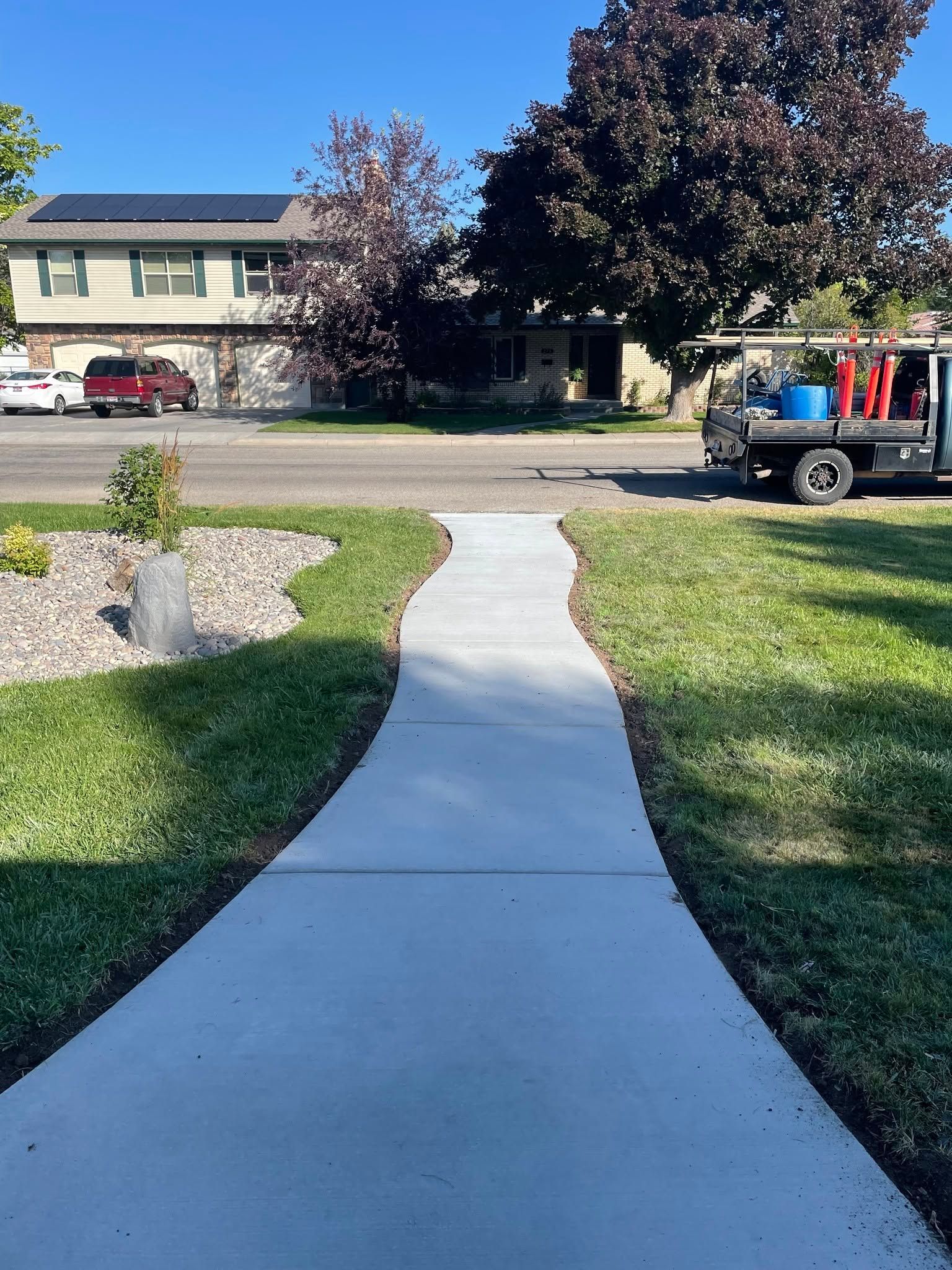 Curved concrete walkway leading across a lawn toward houses, with a truck parked on the right.