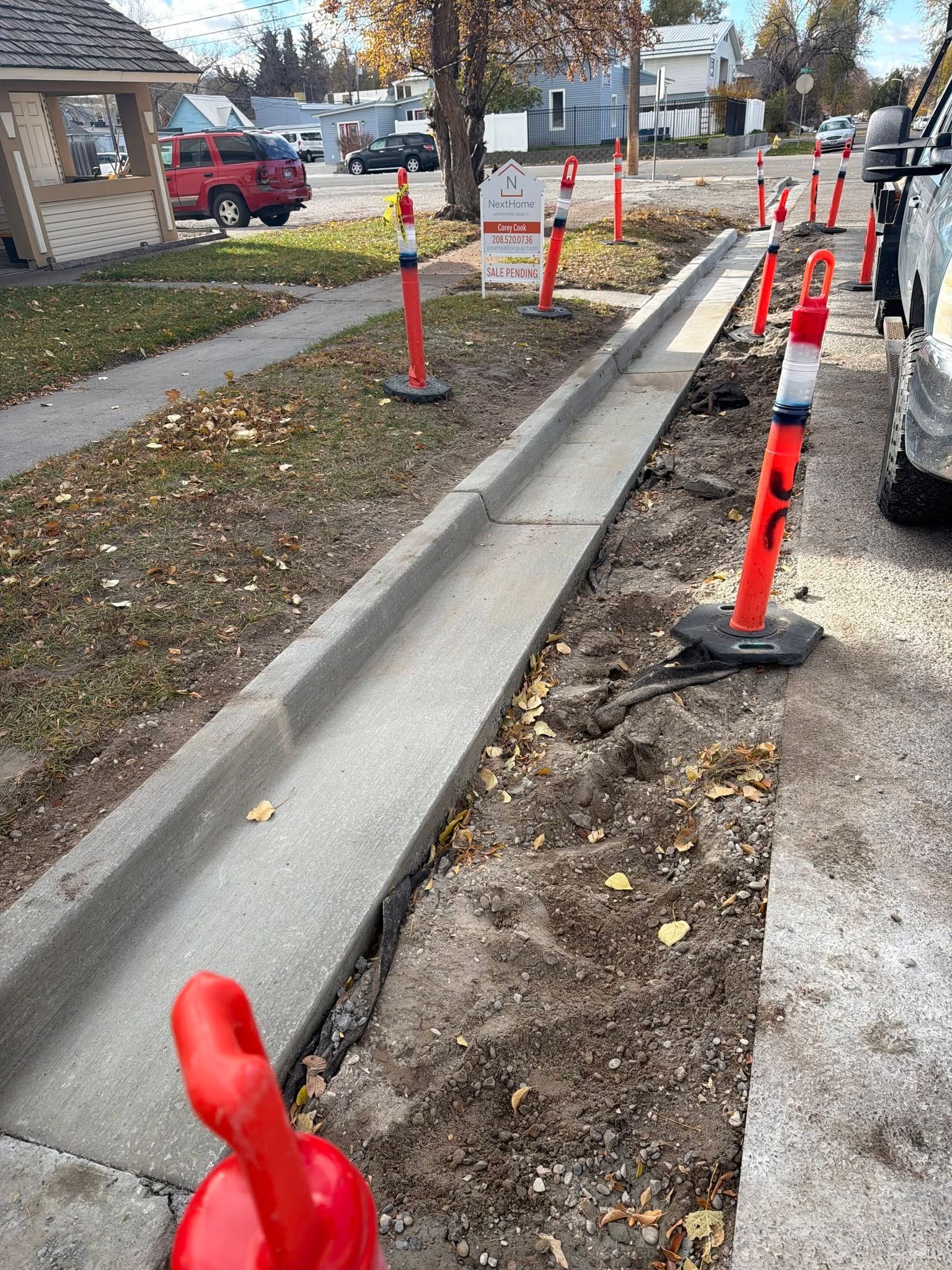 Sidewalk under construction with orange cones, exposed curb, and a parked truck nearby
