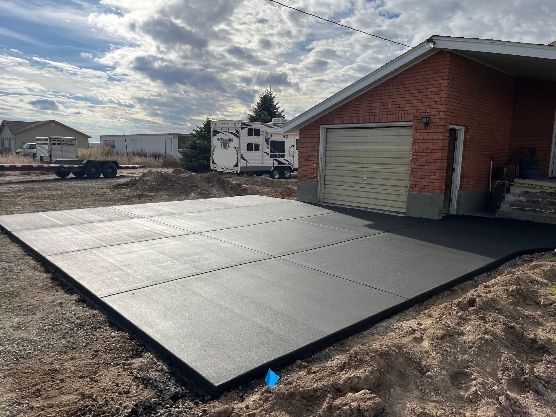 Freshly poured concrete slab beside a brick garage under a cloudy sky