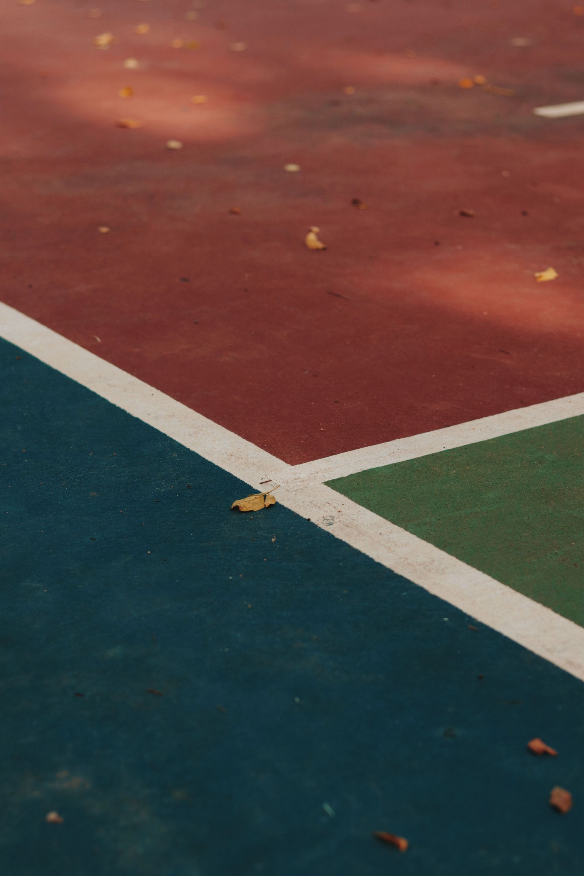 Close-up of a tennis court corner with red, green, and blue painted surfaces divided by white lines