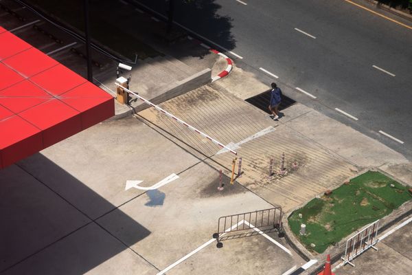 Empty roadside sidewalk with barriers, a red canopy, and a small grassy patch near a street.