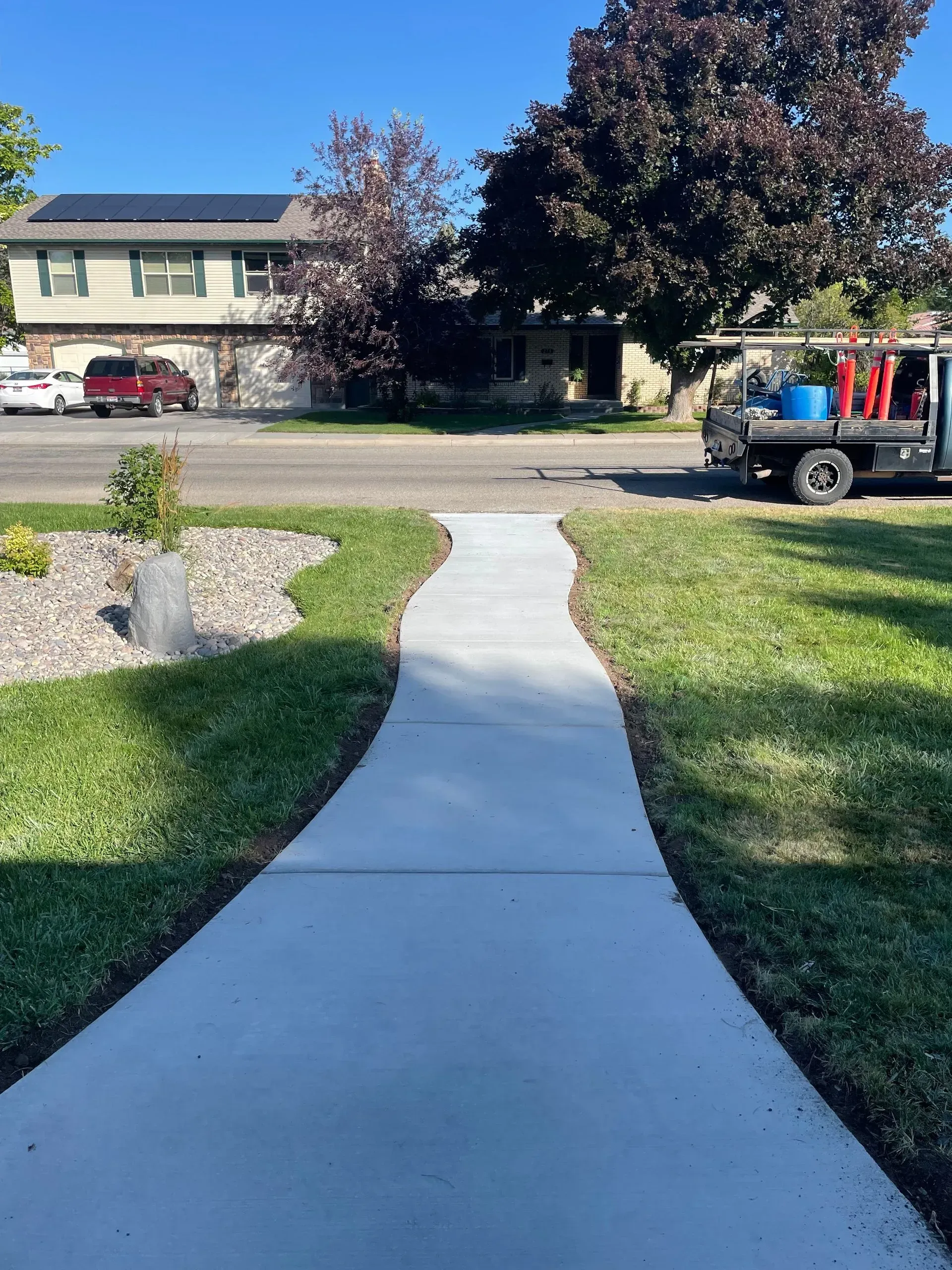 Concrete walkway leading from a lawn to a street with houses and a pickup truck in the background