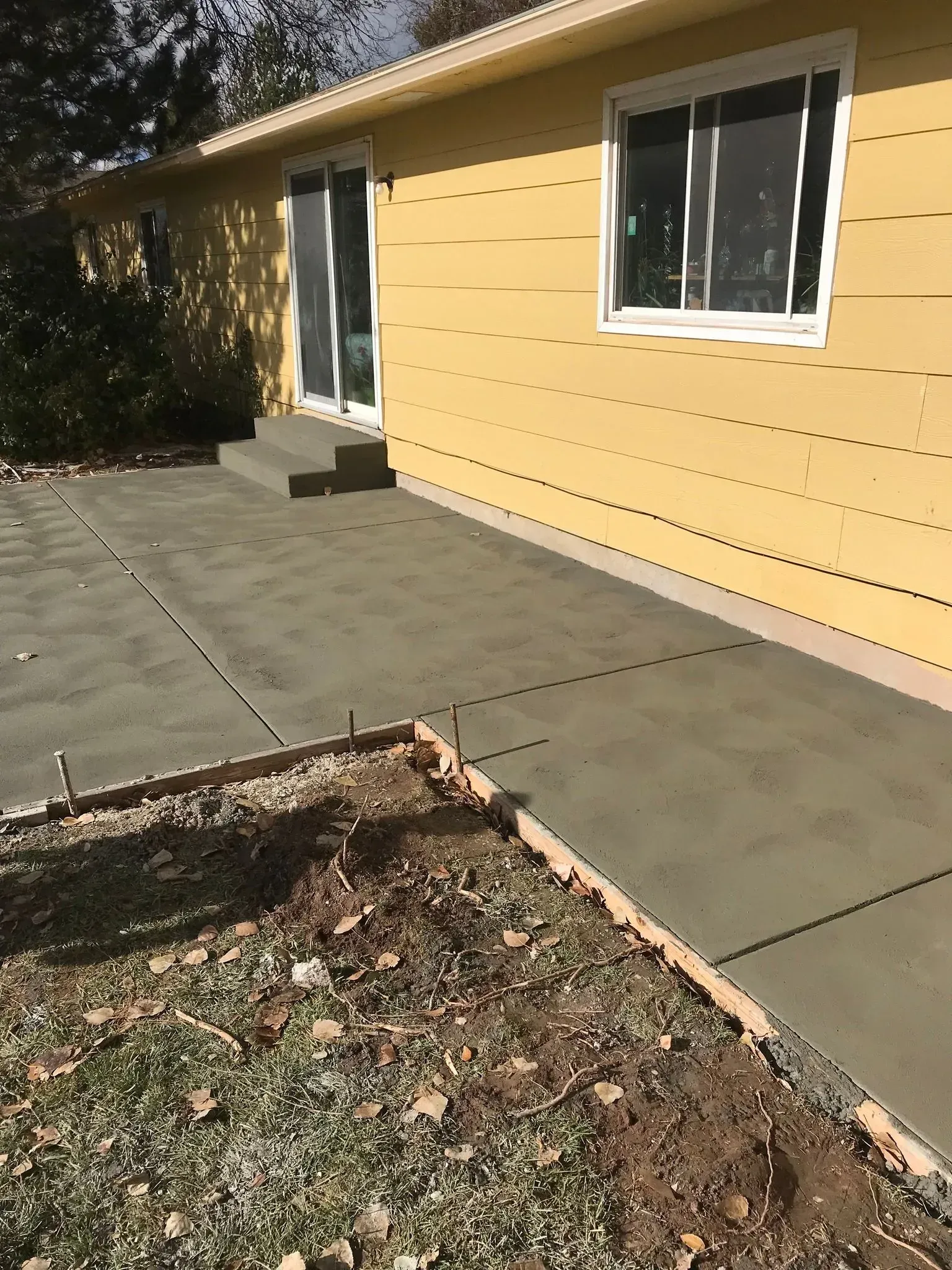 Concrete patio beside a yellow house with white-trimmed windows and a small step leading to a door