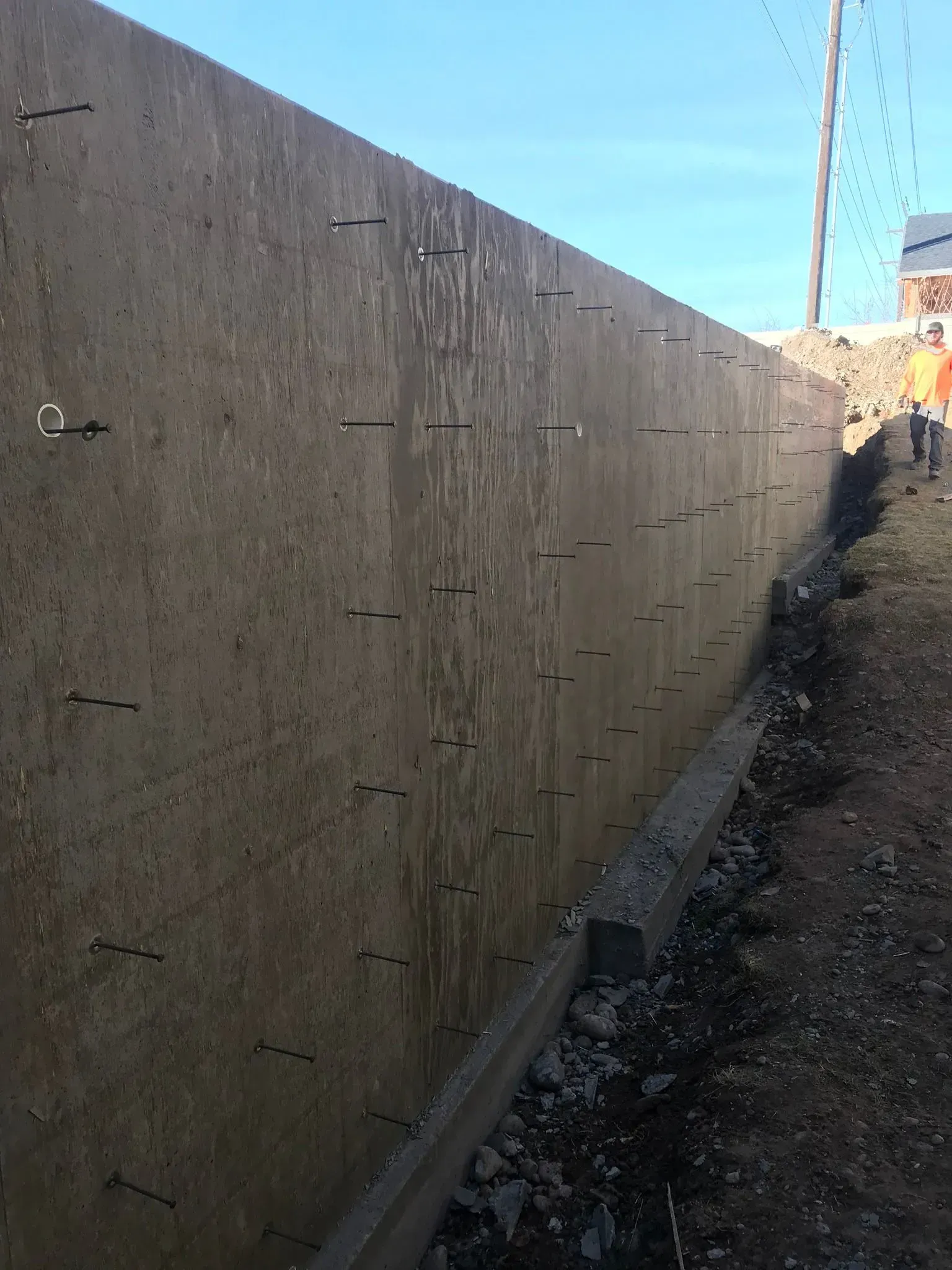 Long concrete retaining wall along a dirt path under blue sky.