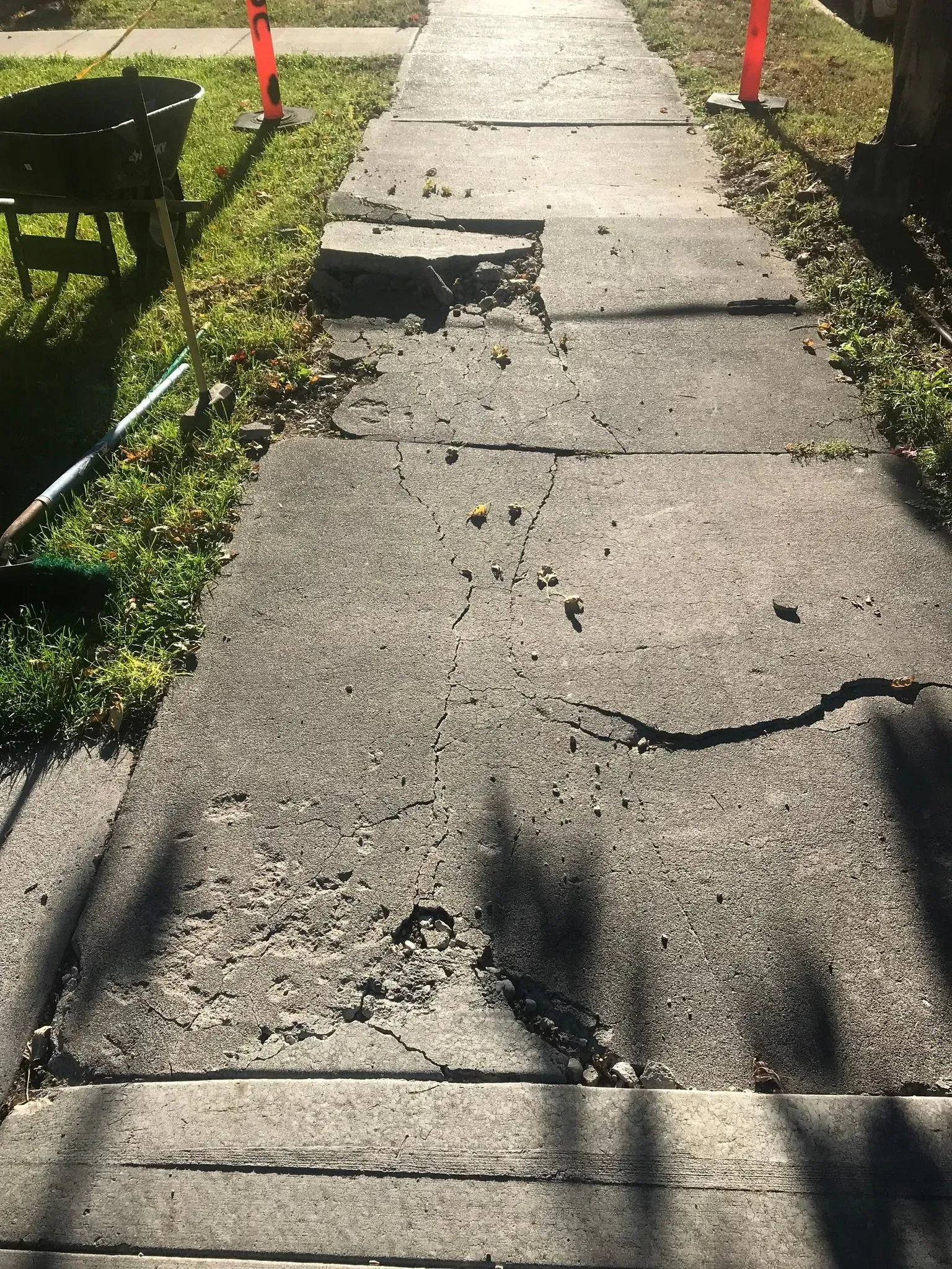 Cracked concrete sidewalk with uneven joints and broken sections in sunlight.