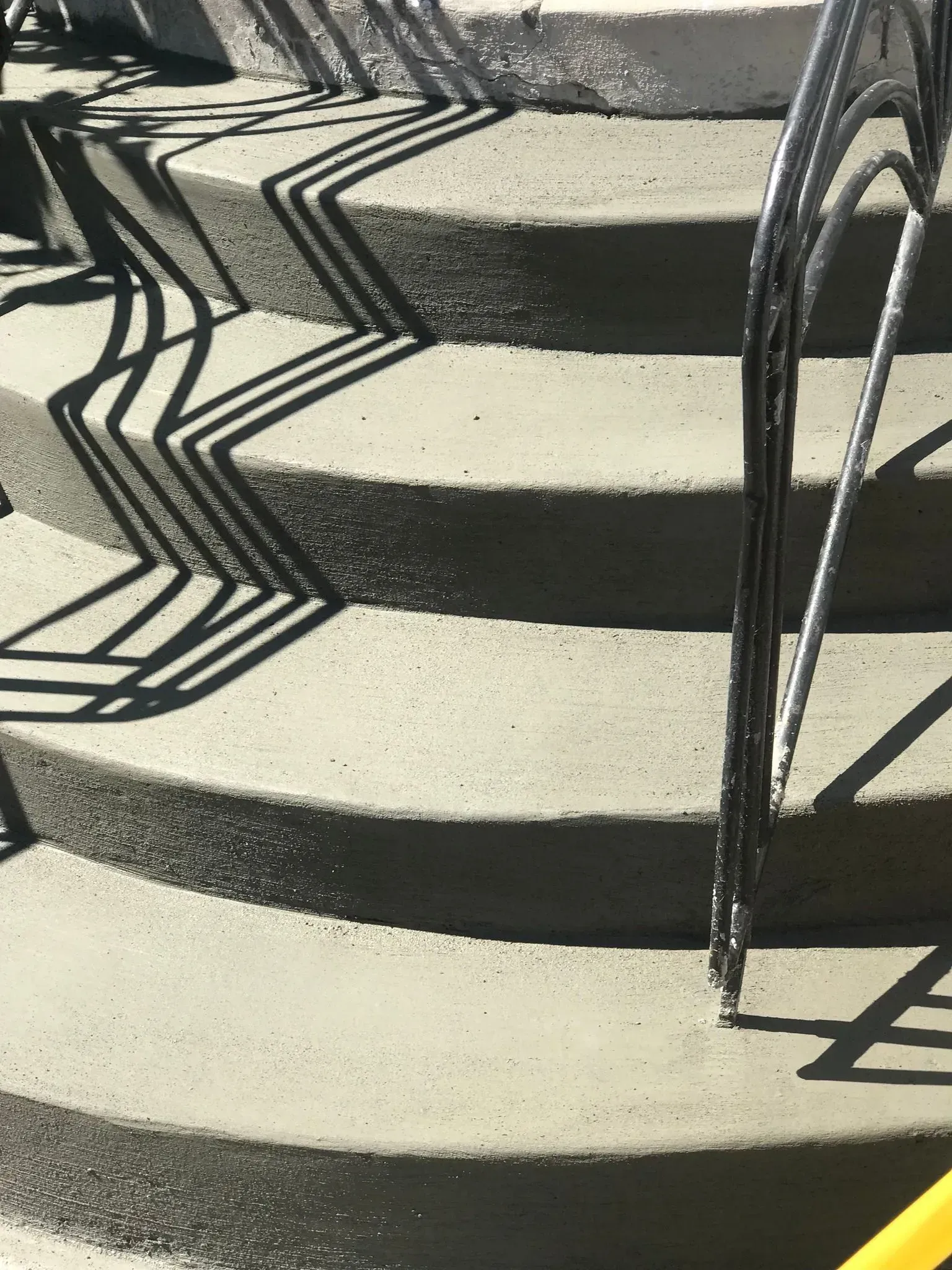 Sunlit concrete steps with curved metal railings casting geometric shadows
