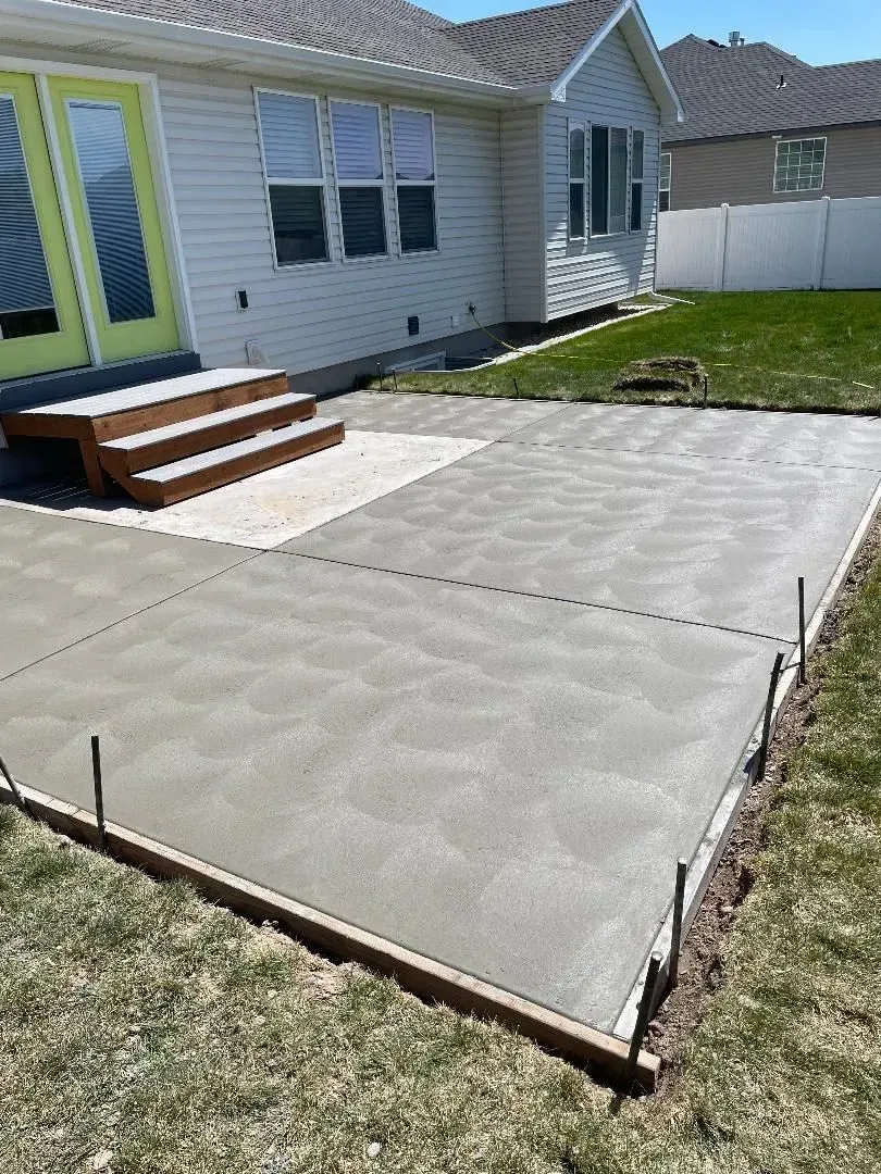 Concrete patio slabs beside a house with lime green door and small wooden steps, next to a lawn.