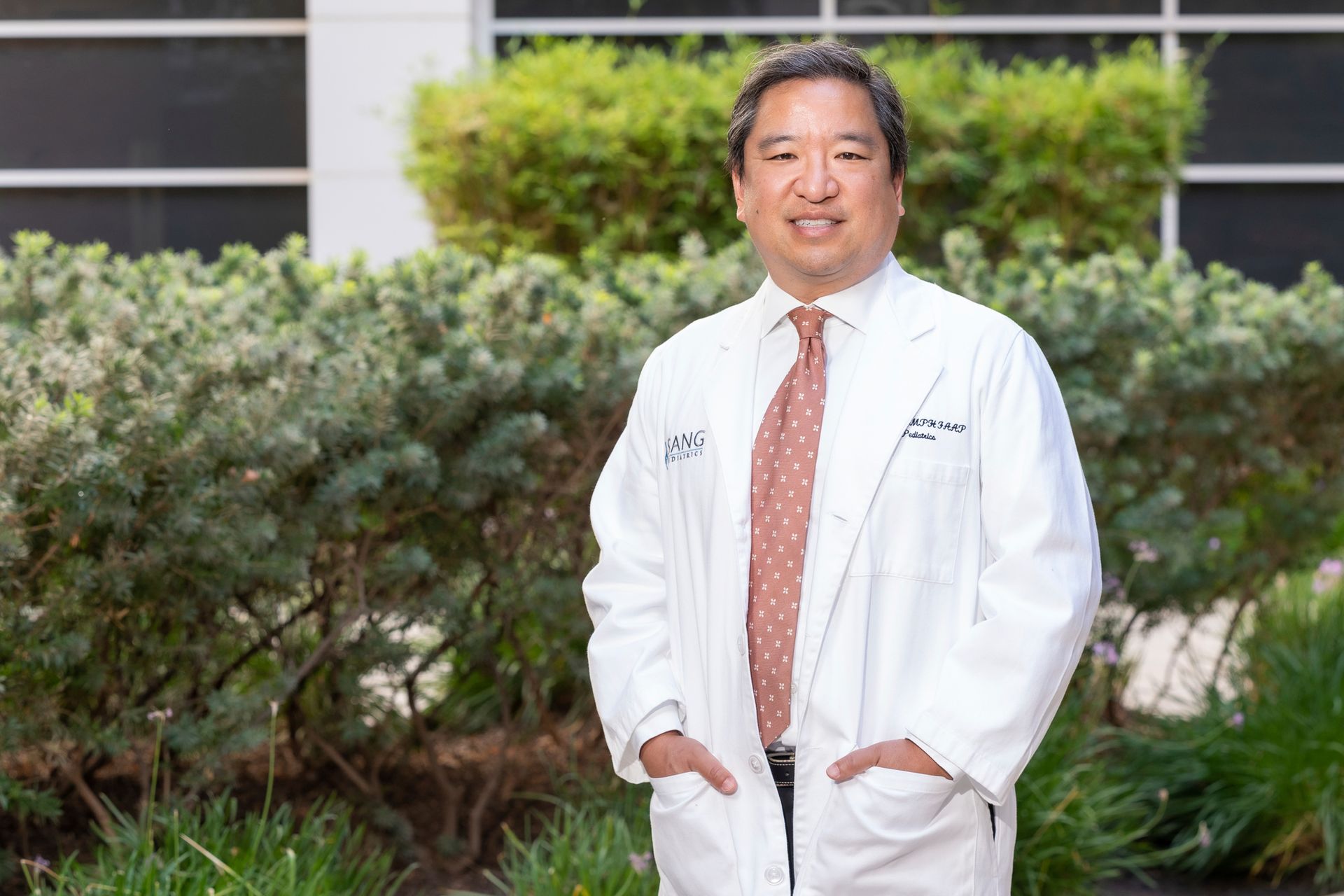A man in a white coat and tie is standing in front of a building.