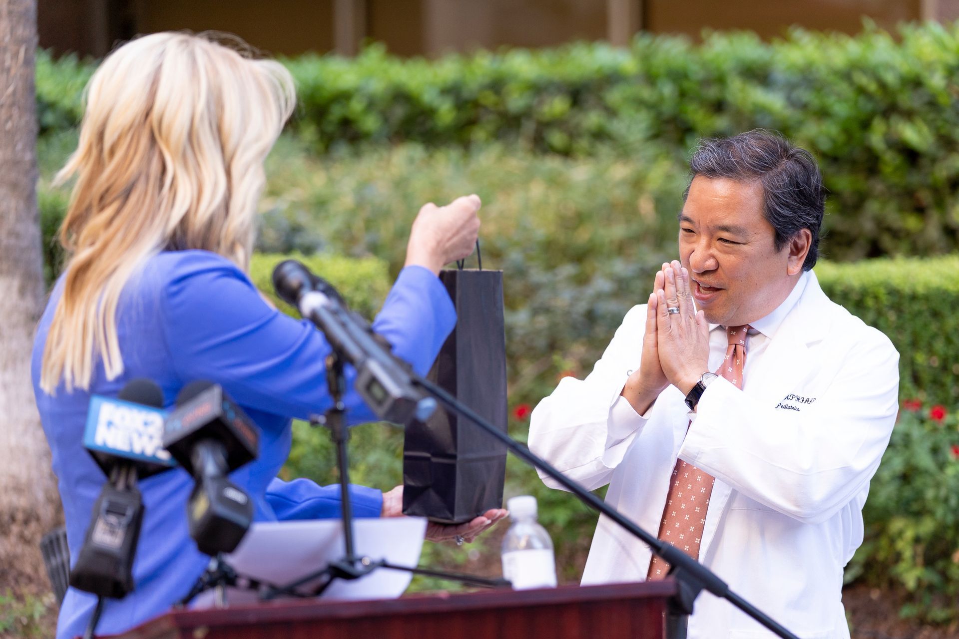 A man in a white coat is giving a gift to a woman in front of a podium.