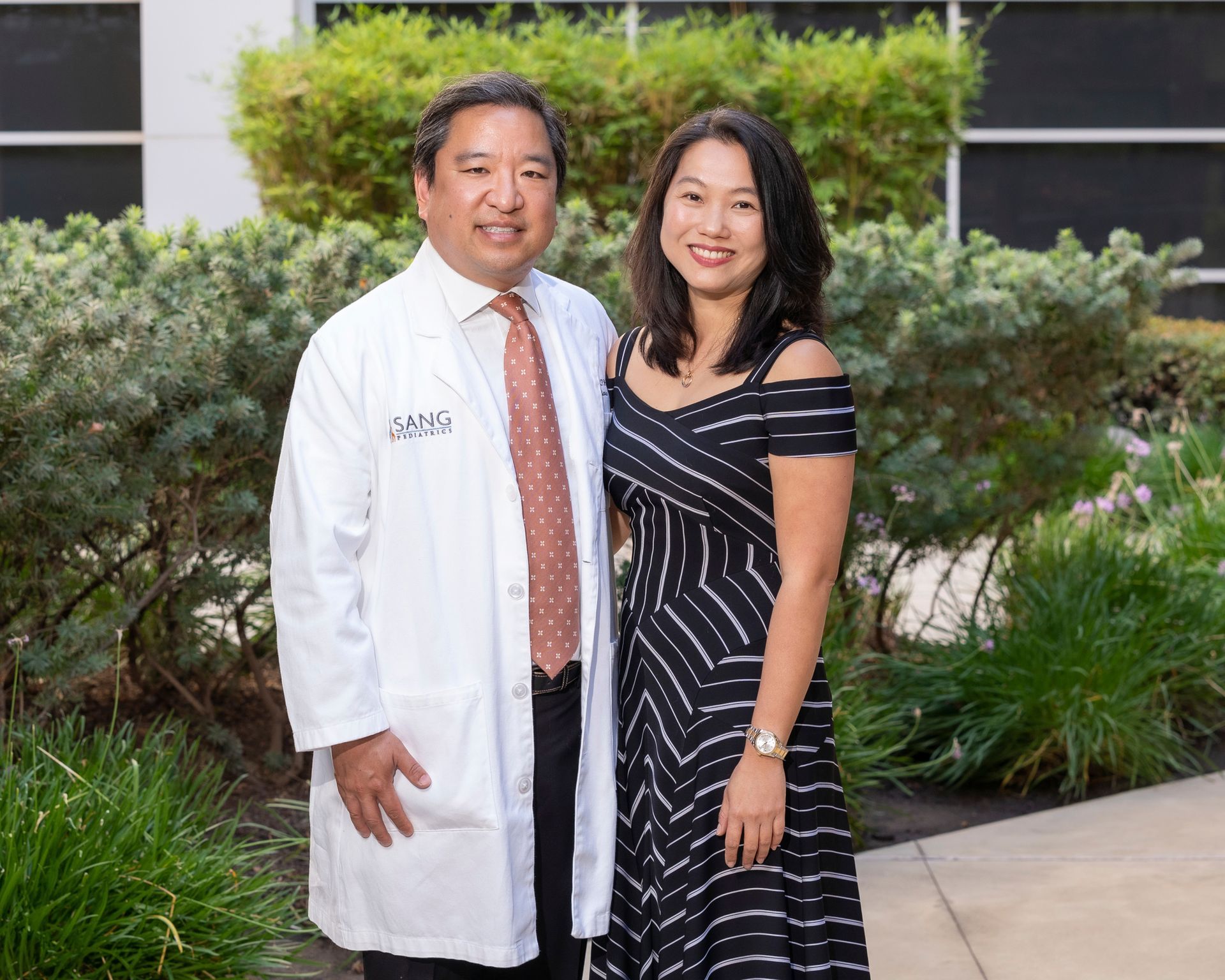 A man in a white coat and tie is standing next to a woman in a black dress.