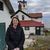 A woman is standing in front of a house with a red roof.