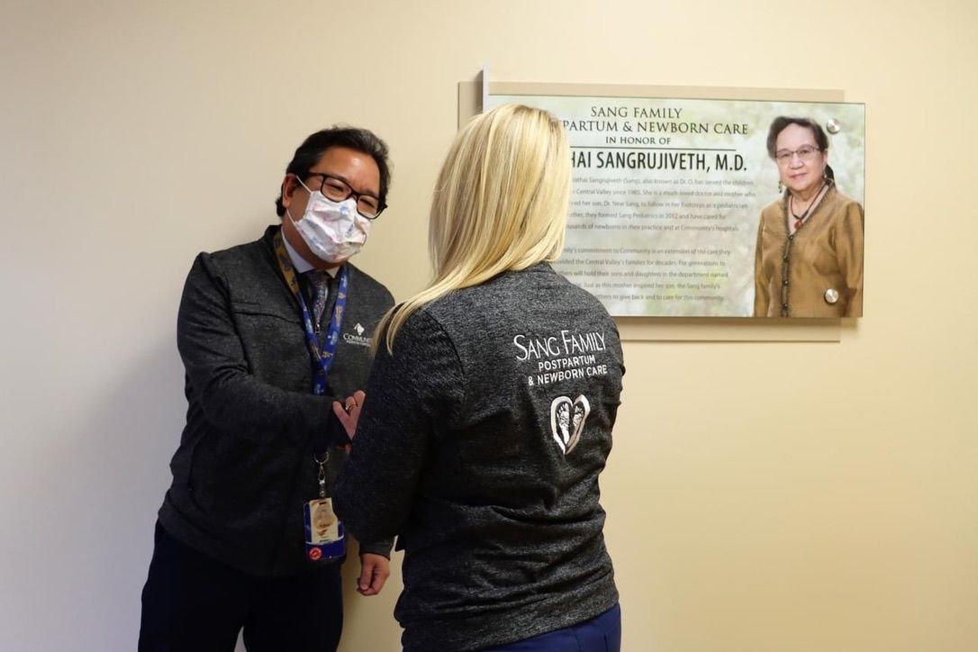 A man wearing a mask is talking to a woman in a room.