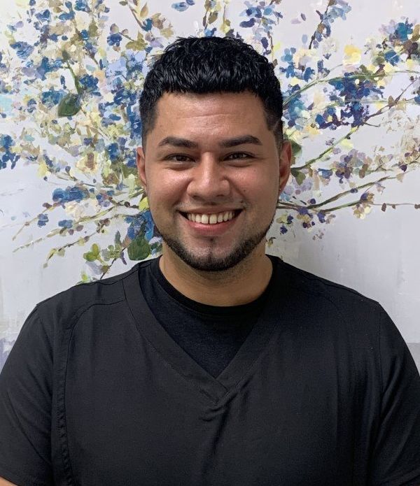 A man with a beard is smiling in front of a painting of flowers.