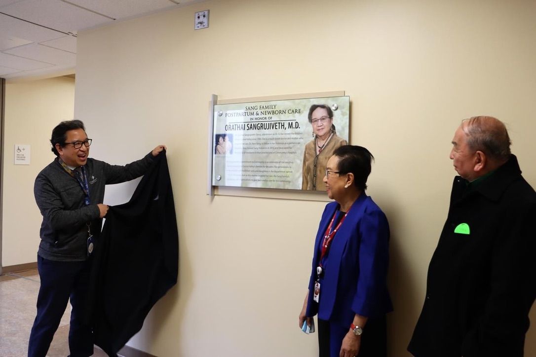 A man and two women are standing in front of a plaque on a wall.